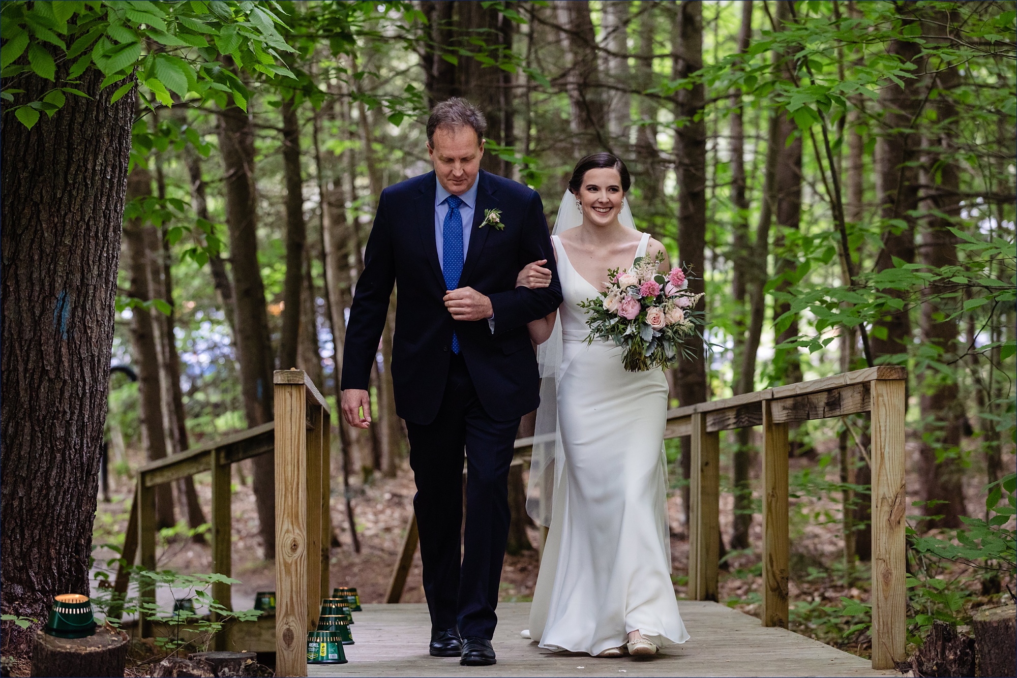 The bride comes down the aisle with her father at her wooded wedding ceremony