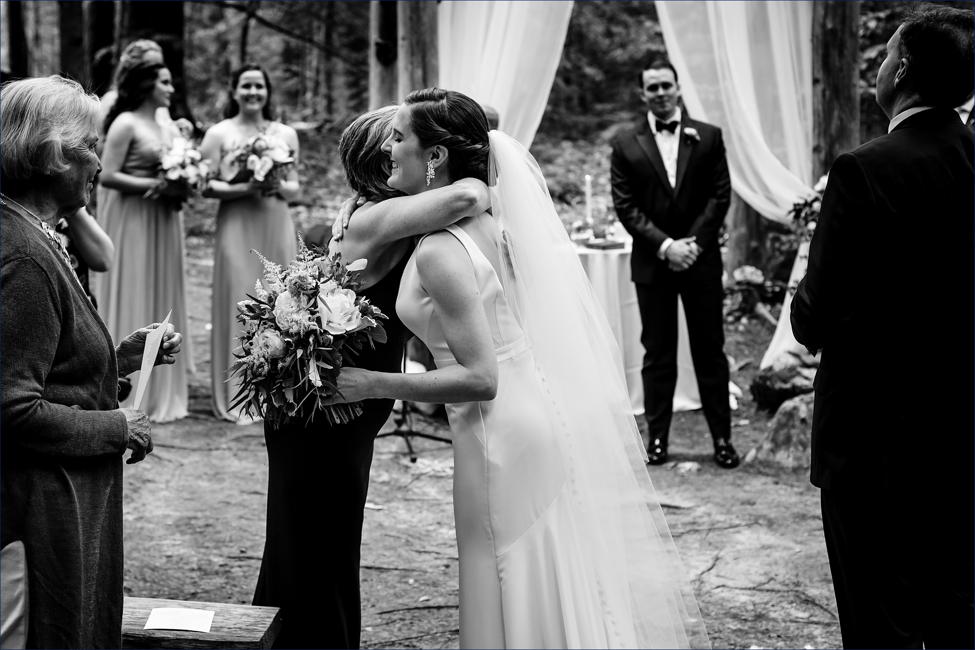 The bride hugs her tearful mom as she comes into the wedding ceremony in the Maine woods