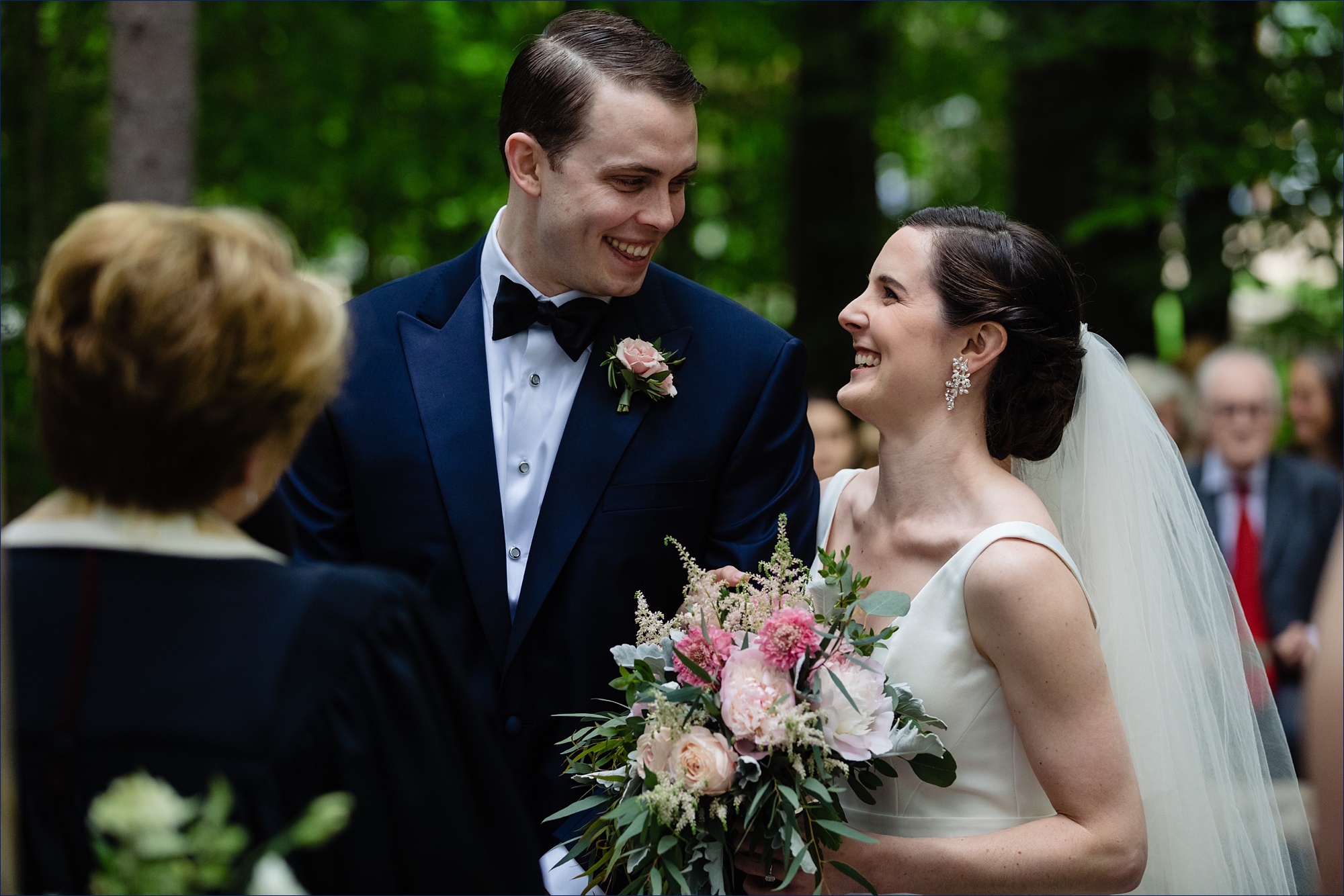 The bride and groom smile at one another at their wooded wedding ceremony in Maine