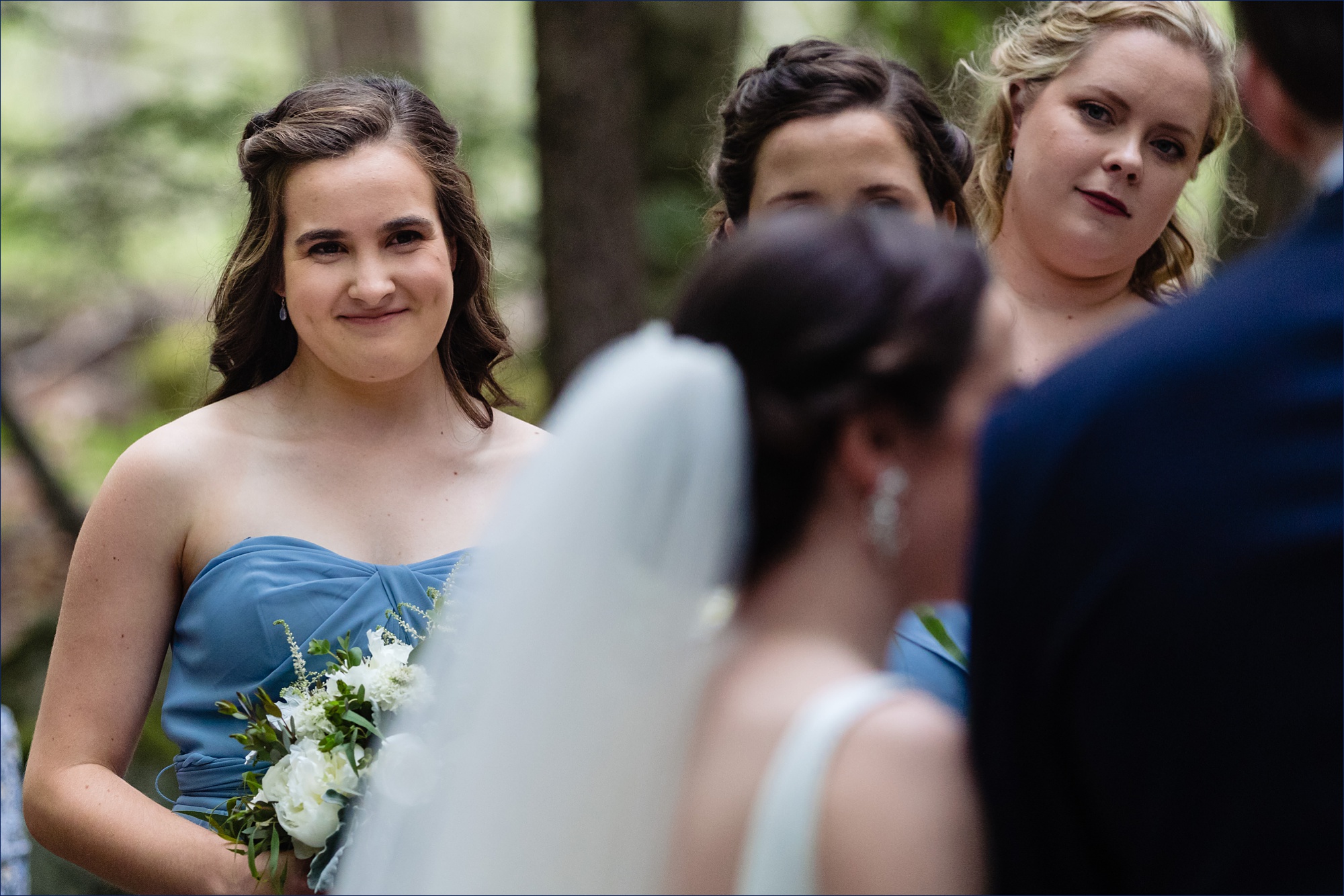 The bridesmaids smile at the couple during the outdoor Maine wedding ceremony