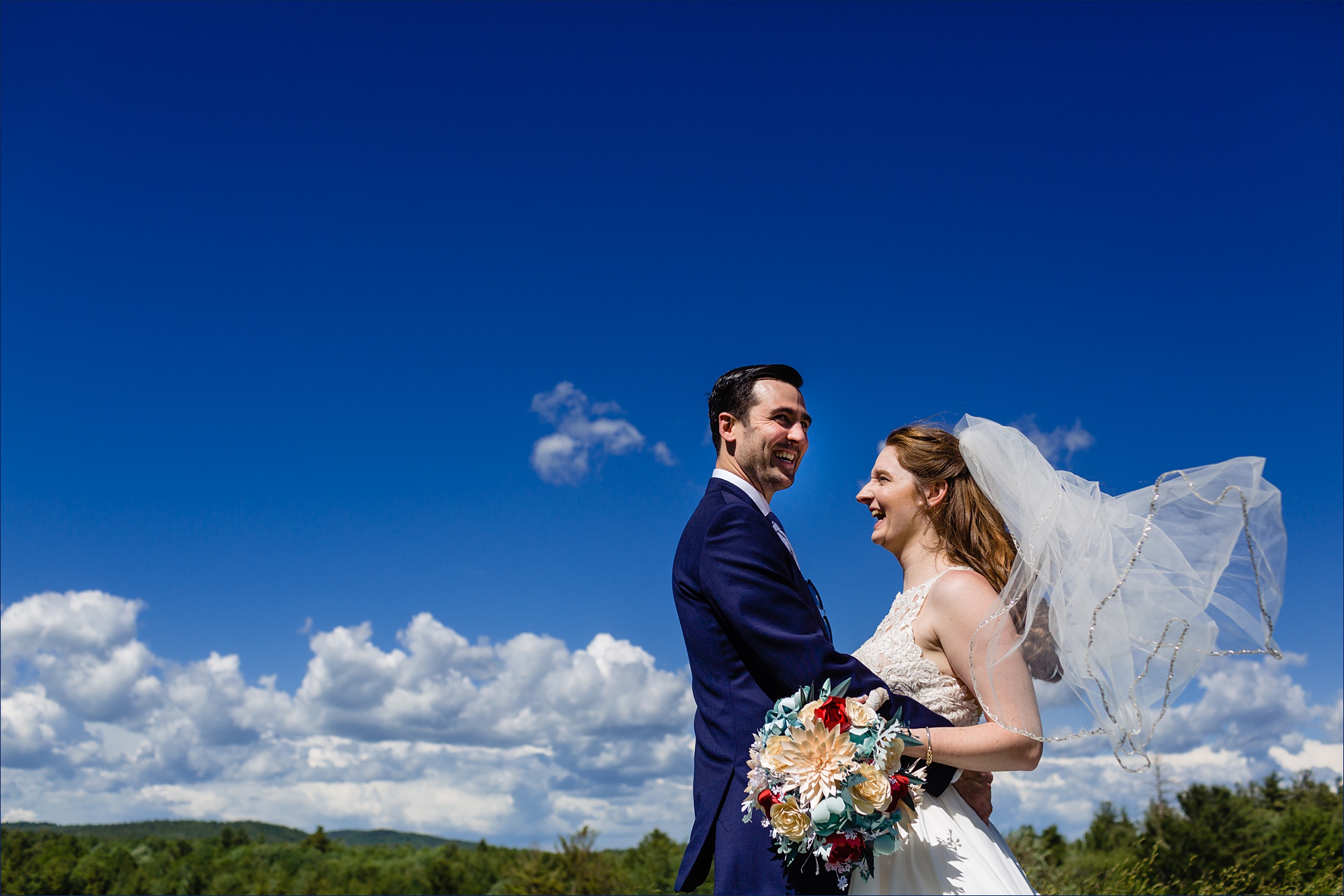 The bride and groom stand close together under a bright blue sky after their NH wedding 