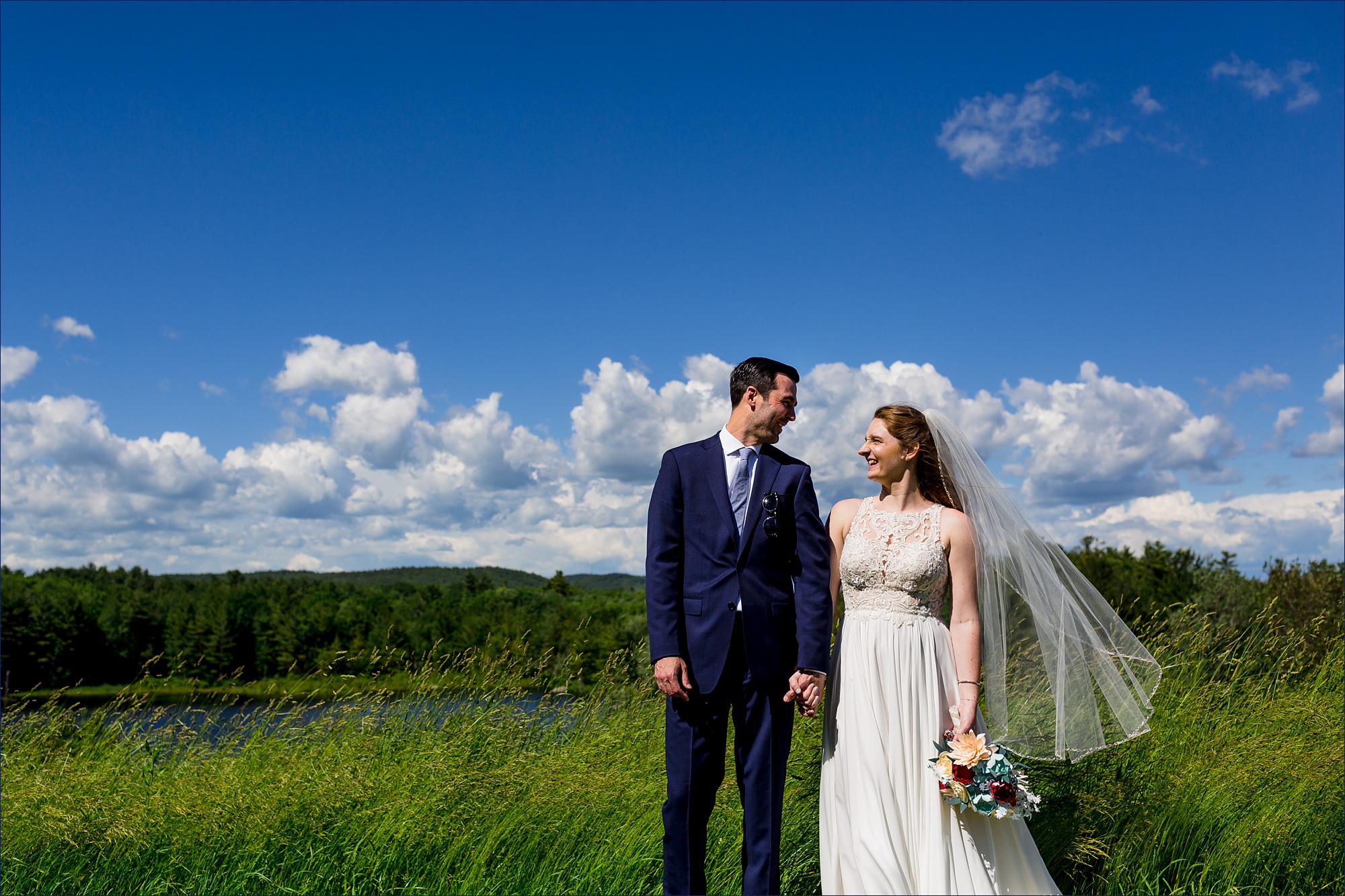 The bride and groom stand close together under a bright blue sky after their NH wedding 