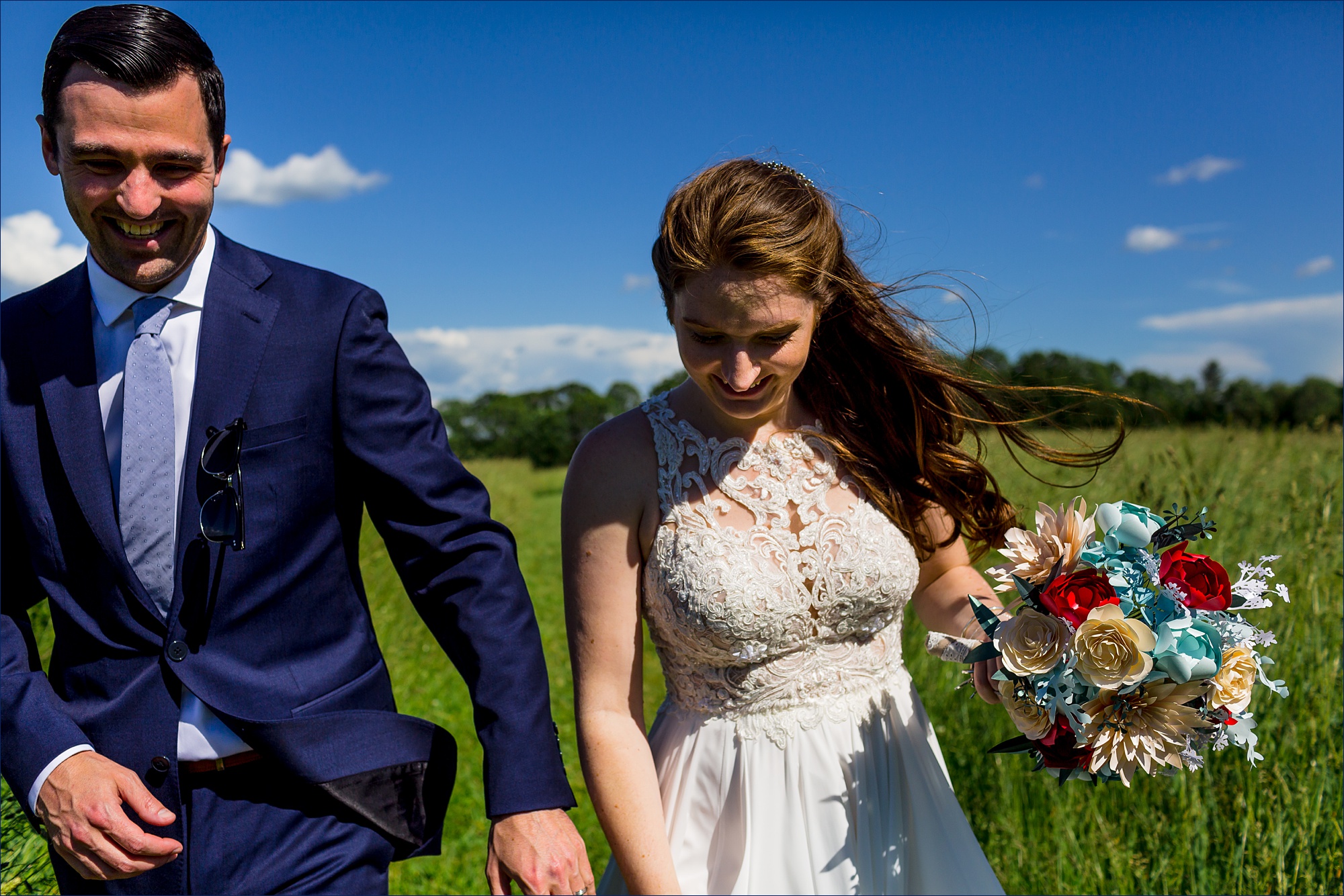 The bride and groom run and laugh after their wedding in a field with a view of the White Mountains