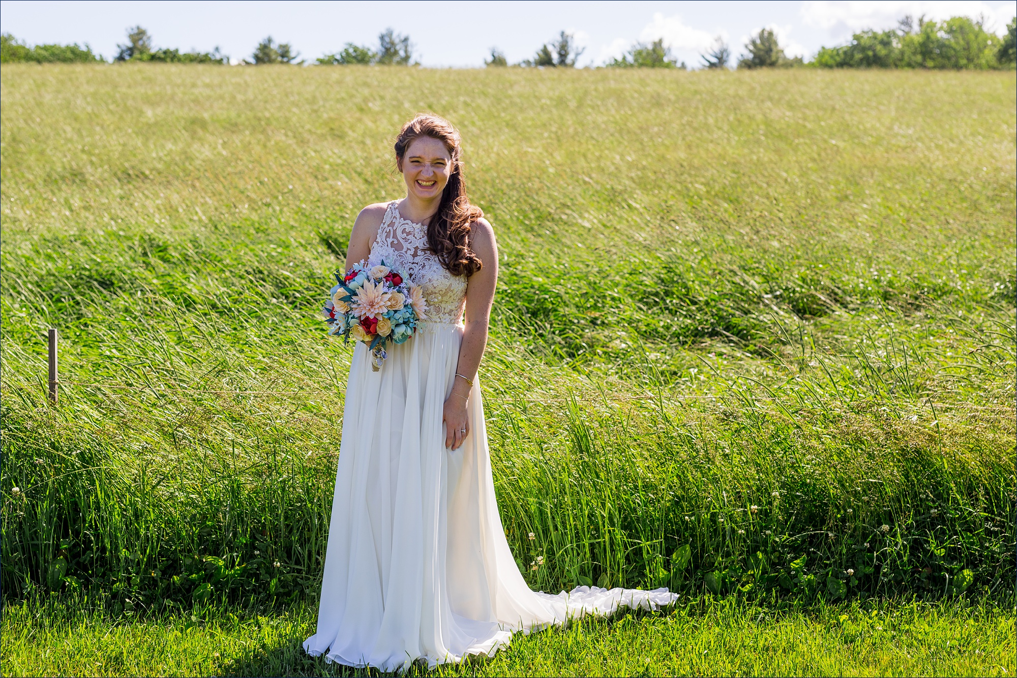 The beautiful bride smiles big in front of the waving tall grass in NH