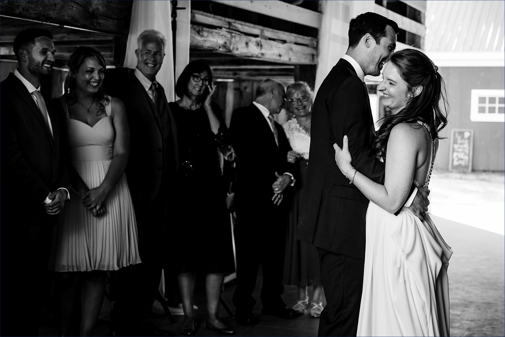 The bride and groom dance together at the reception in the barn at Kitz Farm as family smiles