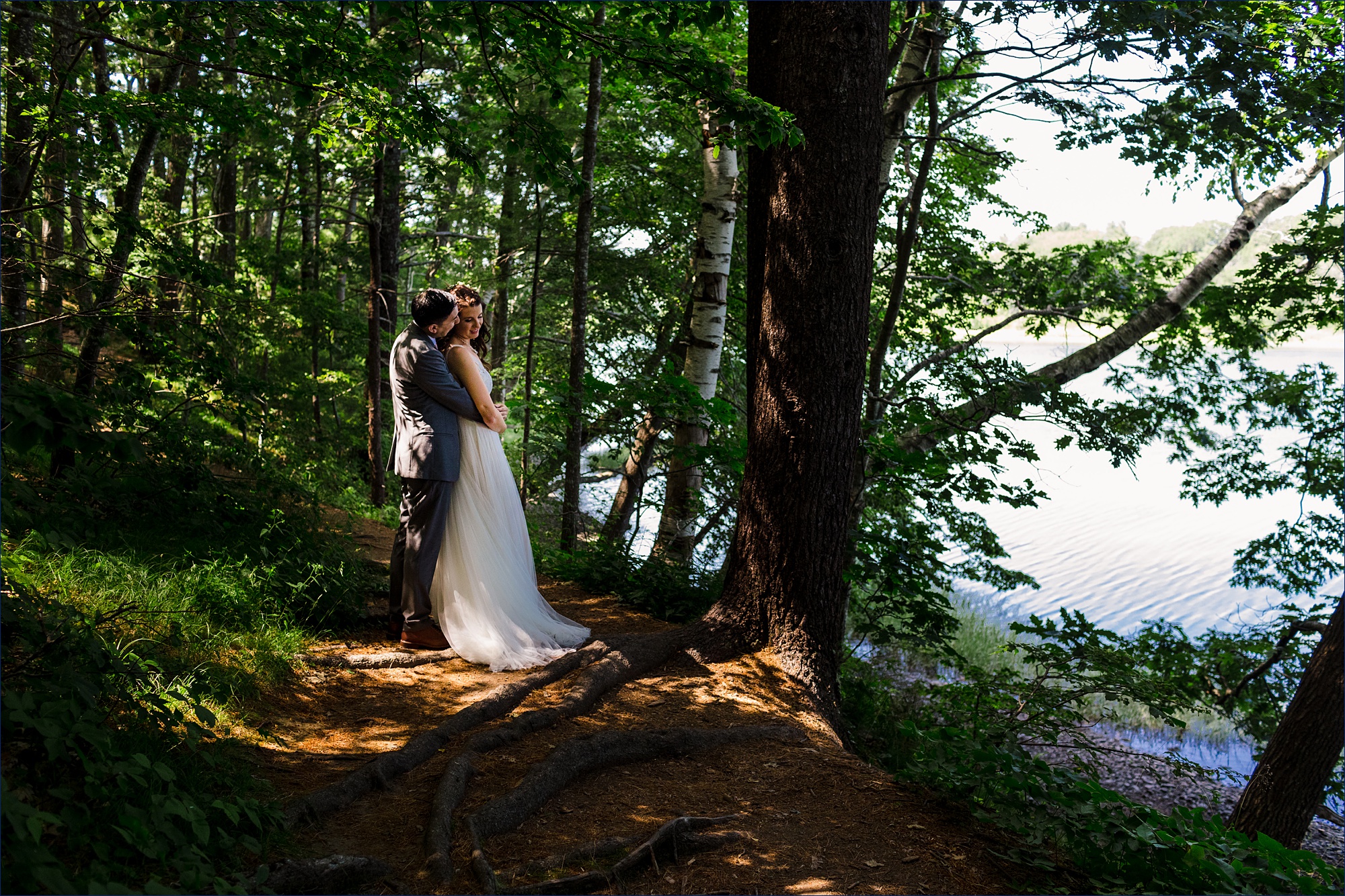 The bride and groom share a kiss while he holds her in the cool woods on their York Maine Wedding day