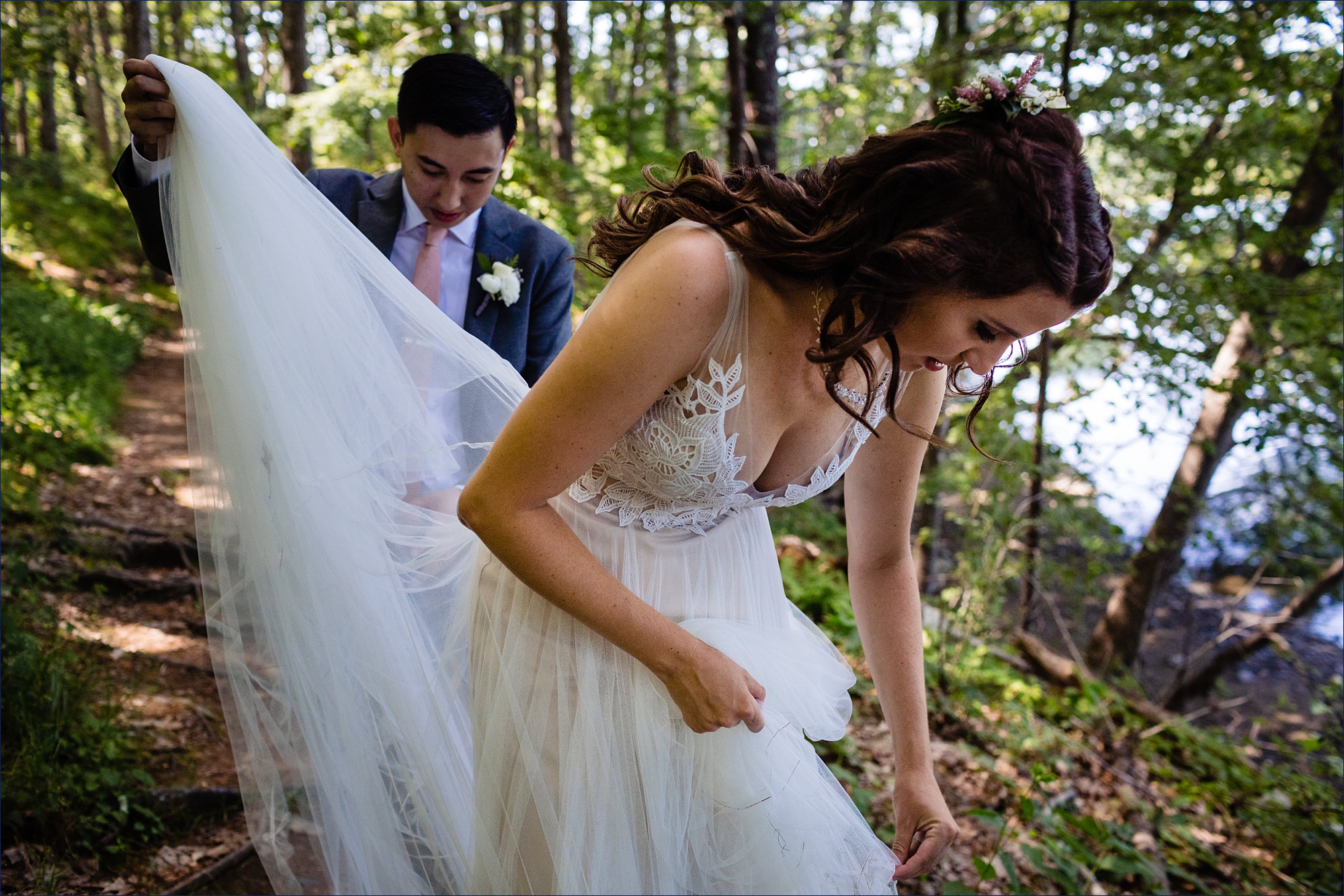 The groom helps pick leaves out of the bride's dress after walking through the woods
