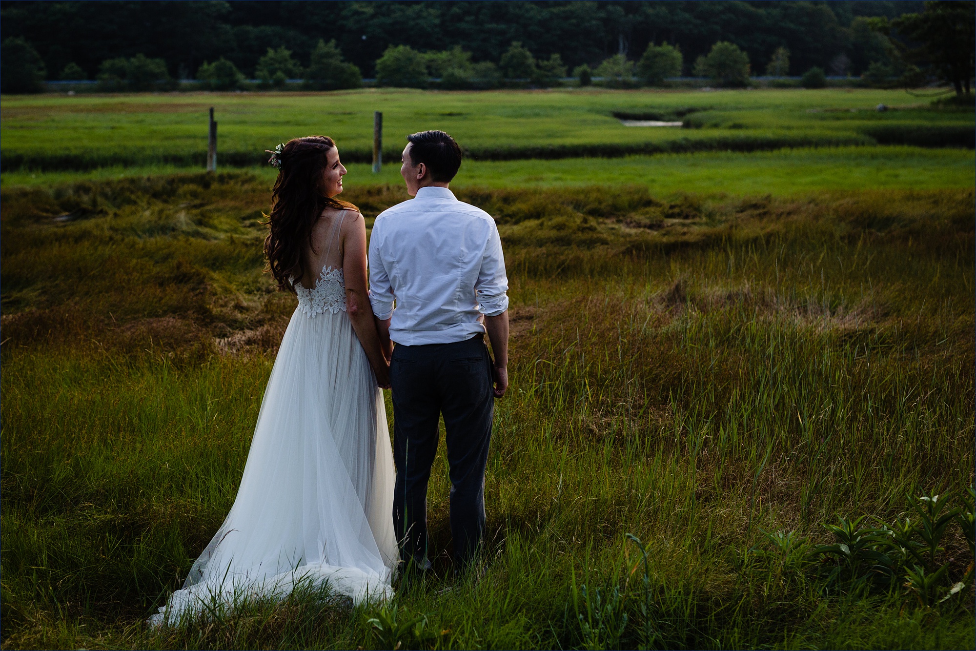 The bride and groom hold hands while out in the sea grass on their southern Maine wedding