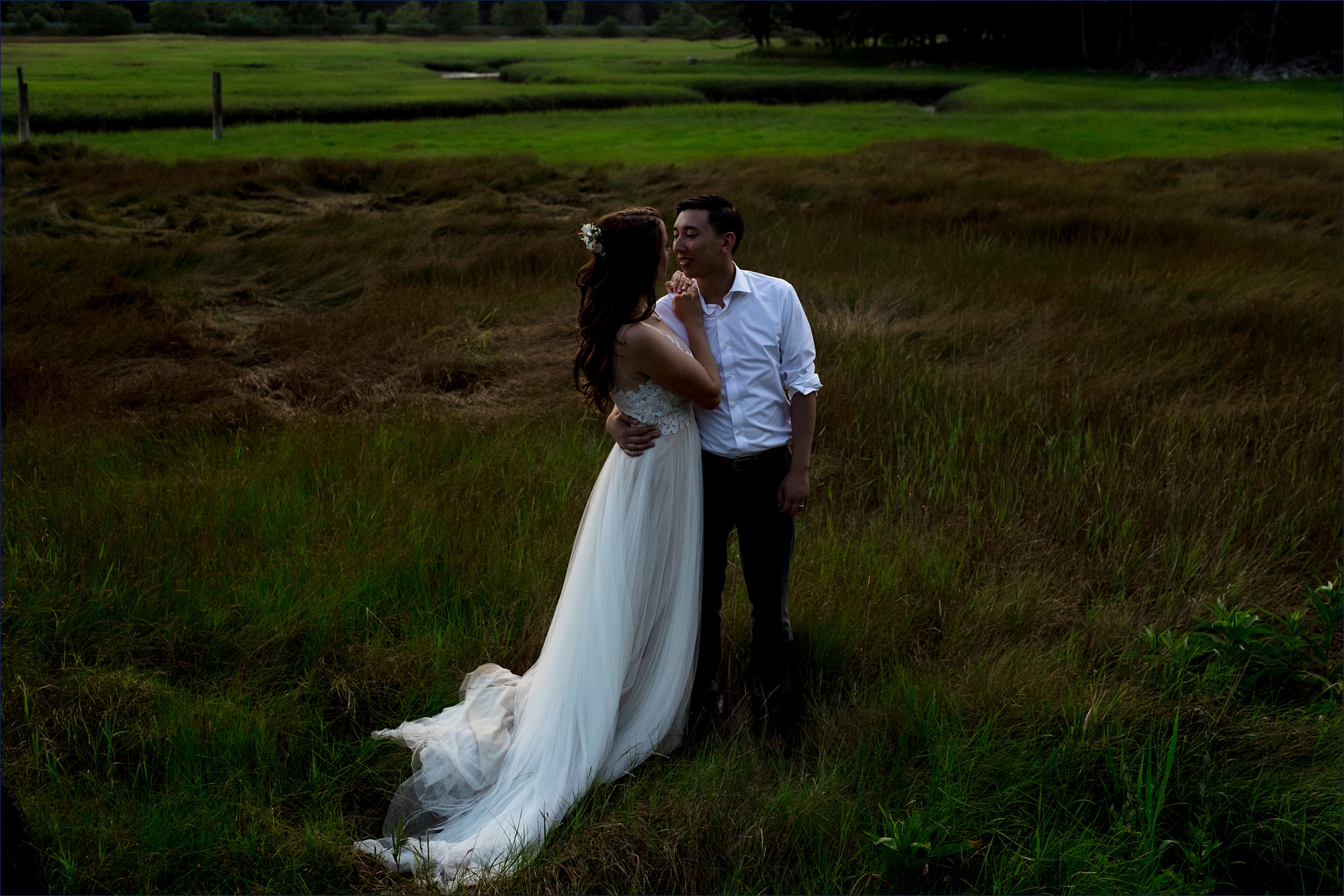 The bride and groom get close to one another out in the sea grass on their southern Maine wedding