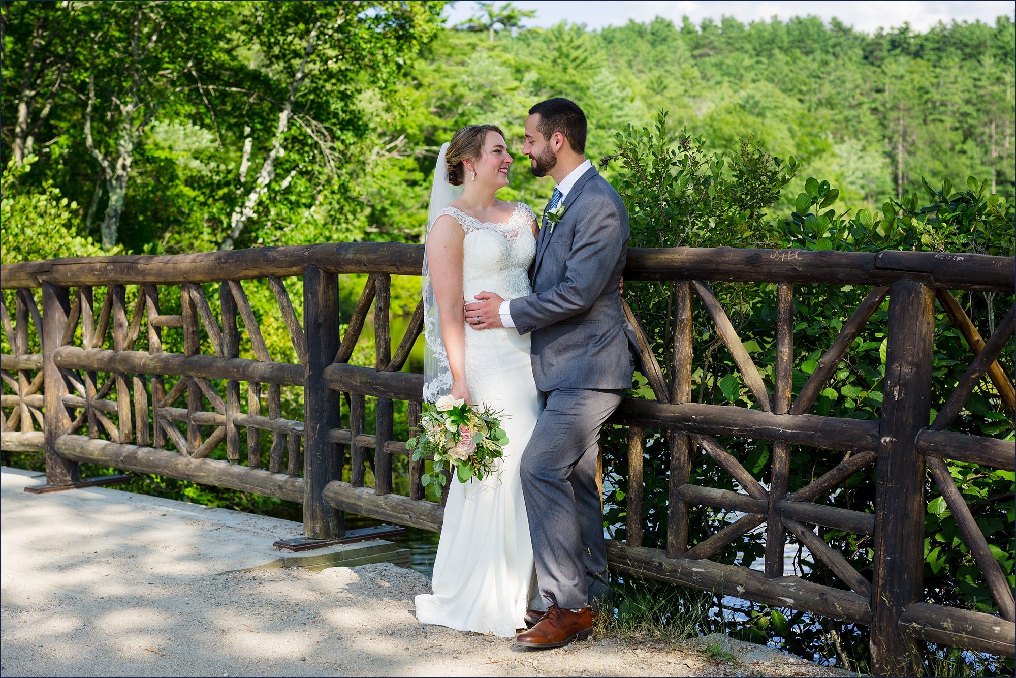 The bride and groom smile at one another on the bridge over Lake Chocorua NH