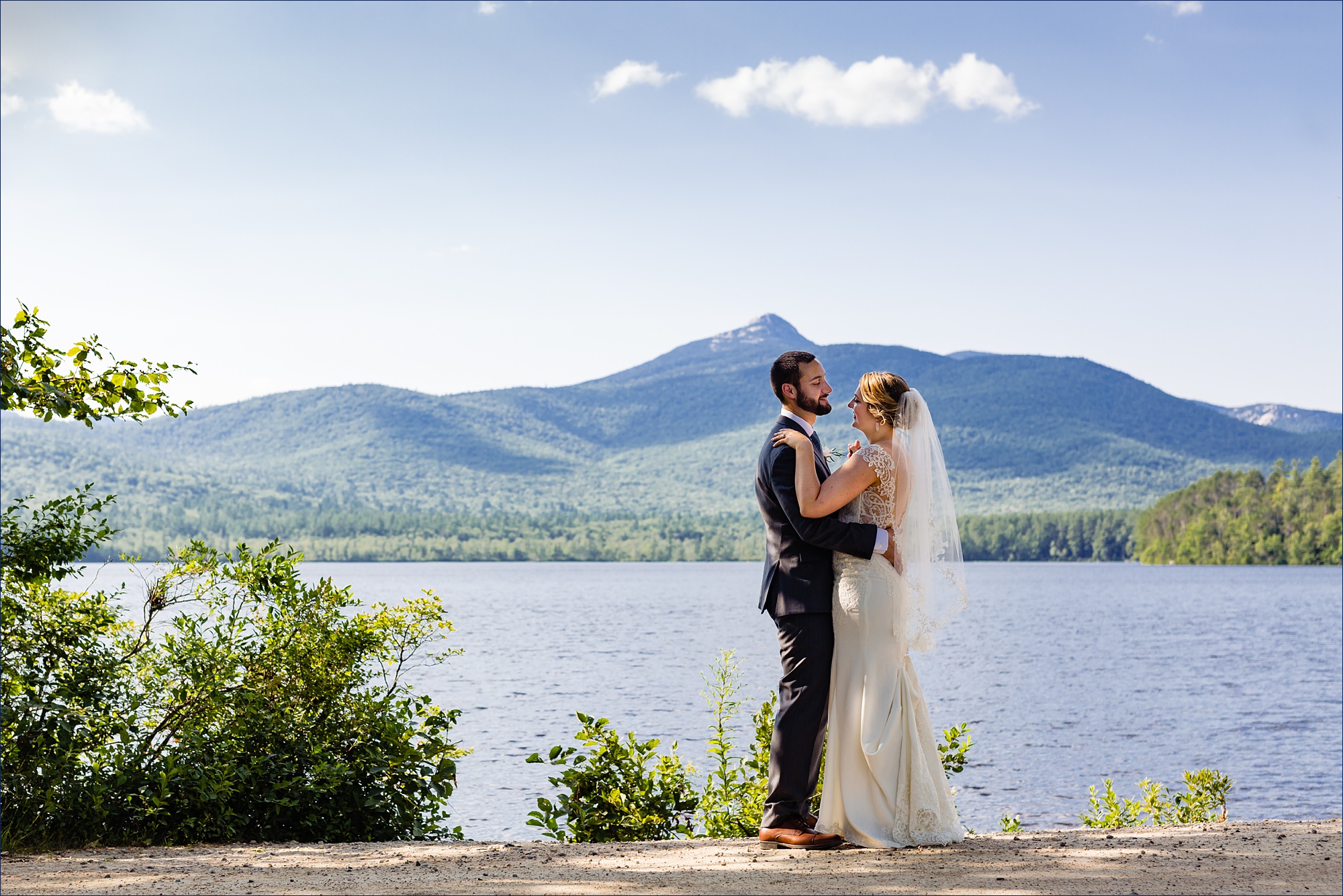The bride and groom get close to one another in front of Mount Chocorua and Chocorua Lake in New Hampshire