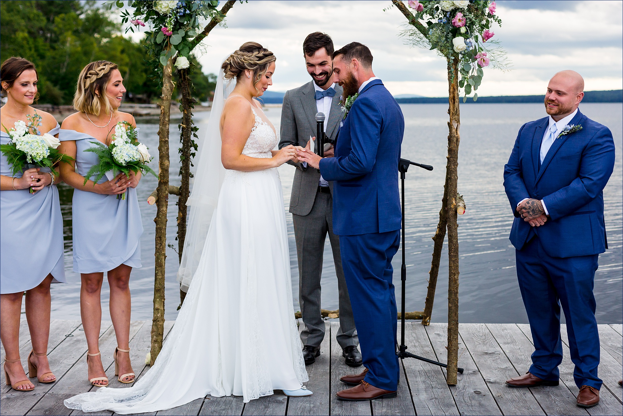 The bride and groom have their ceremony out on a dock overlooking a Maine lake and mountains