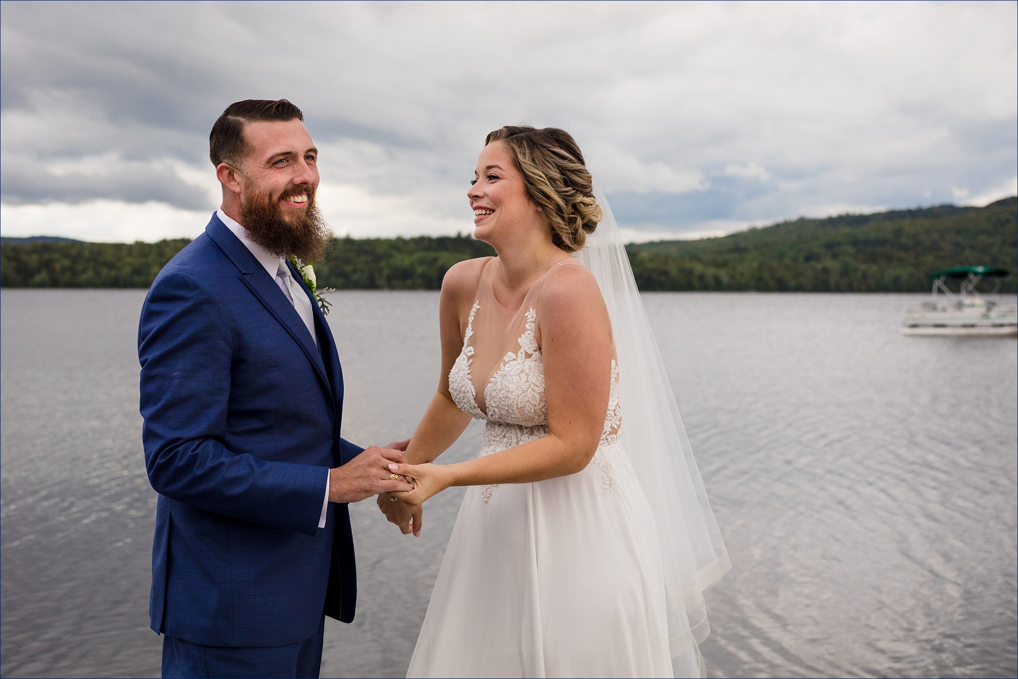 The bride and groom laugh as they hold onto one another after their Maine wedding out on a lake