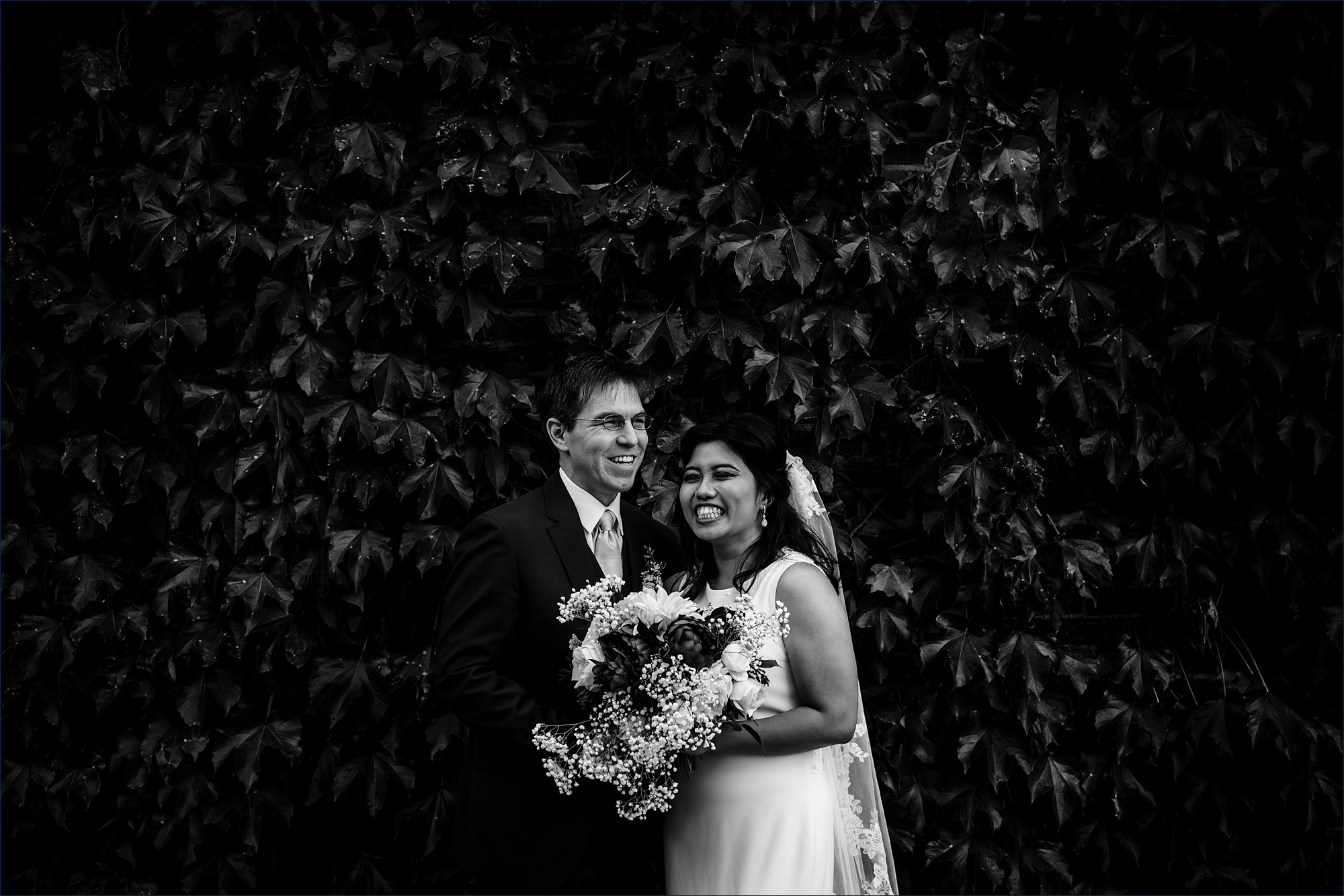 The bride and groom smile big in front of a fall colored ivy wall on the Ivy League campus in NH