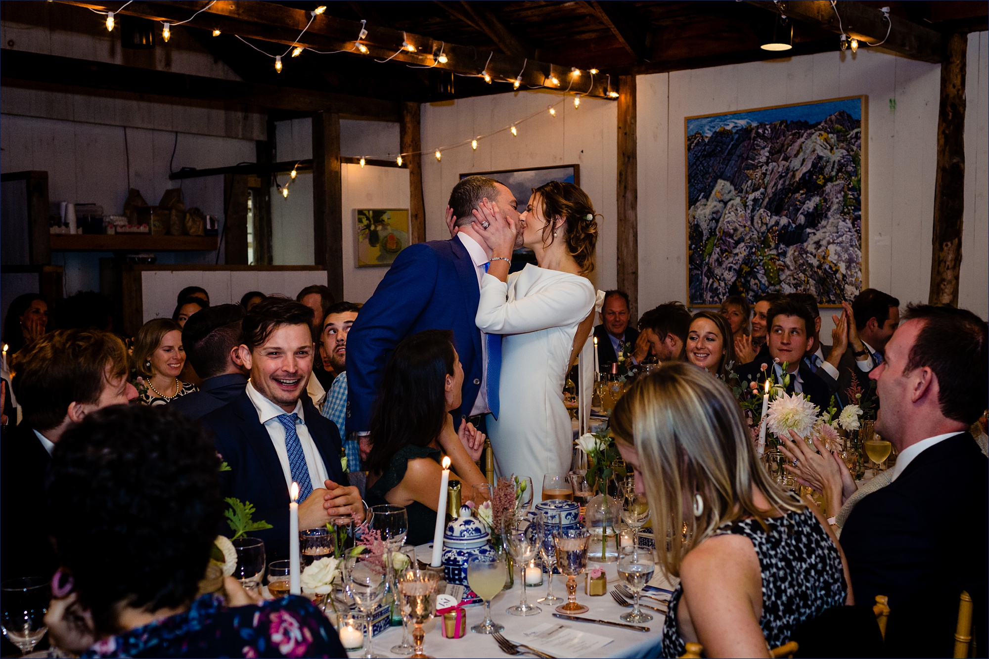 The bride and groom kiss at the dinner table at Islesford Dock Restaurant as the reception is about to start