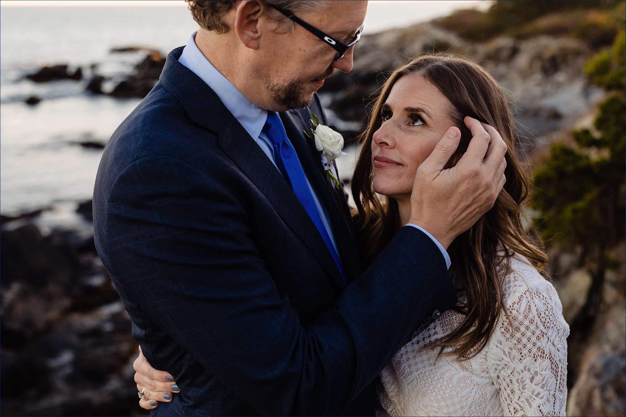 The groom fixes the bride's hair while out on the rocky Maine shores