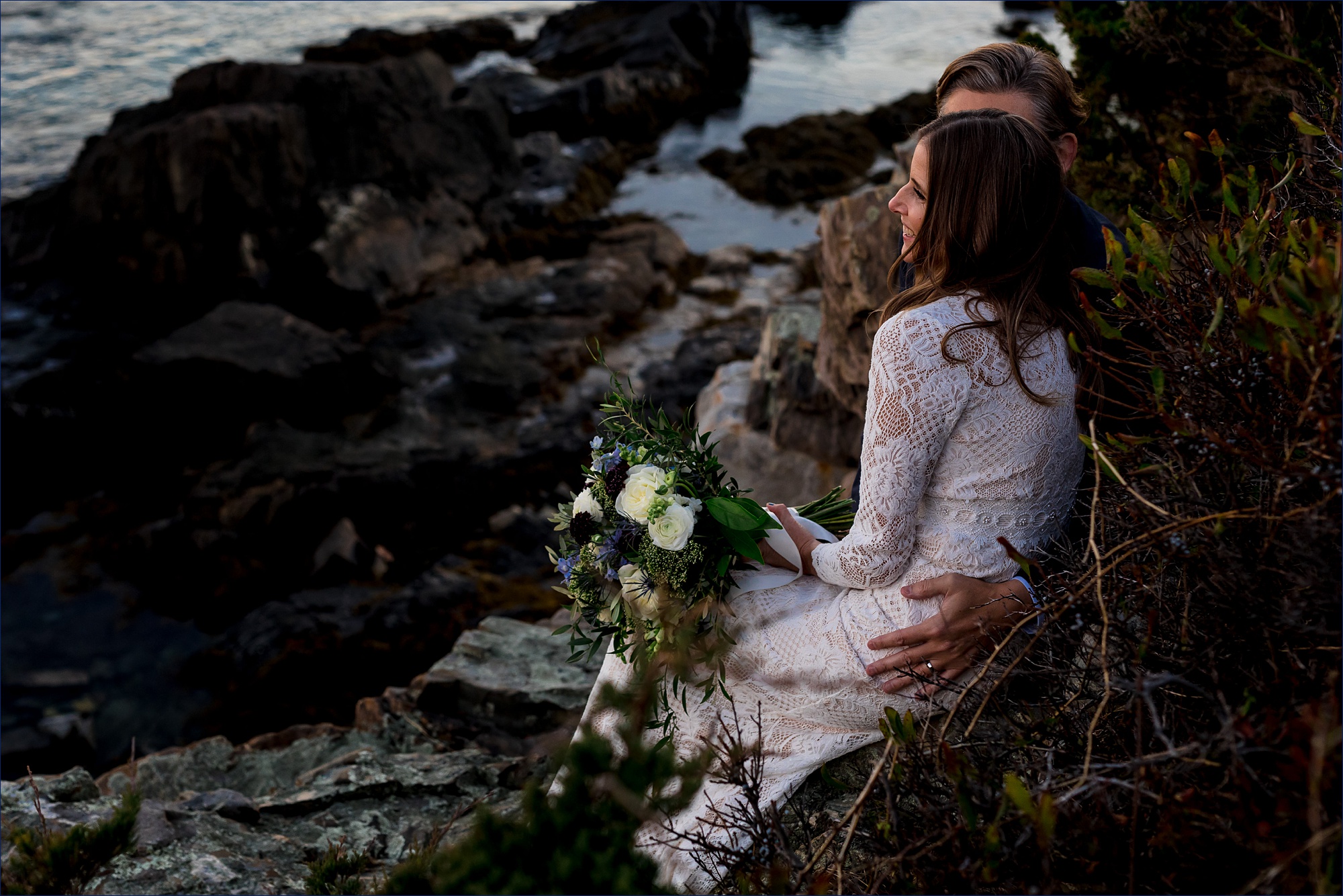 The newlyweds cuddle close on the rocks after their Cape Arundel Inn wedding day in Kennebunkport Maine