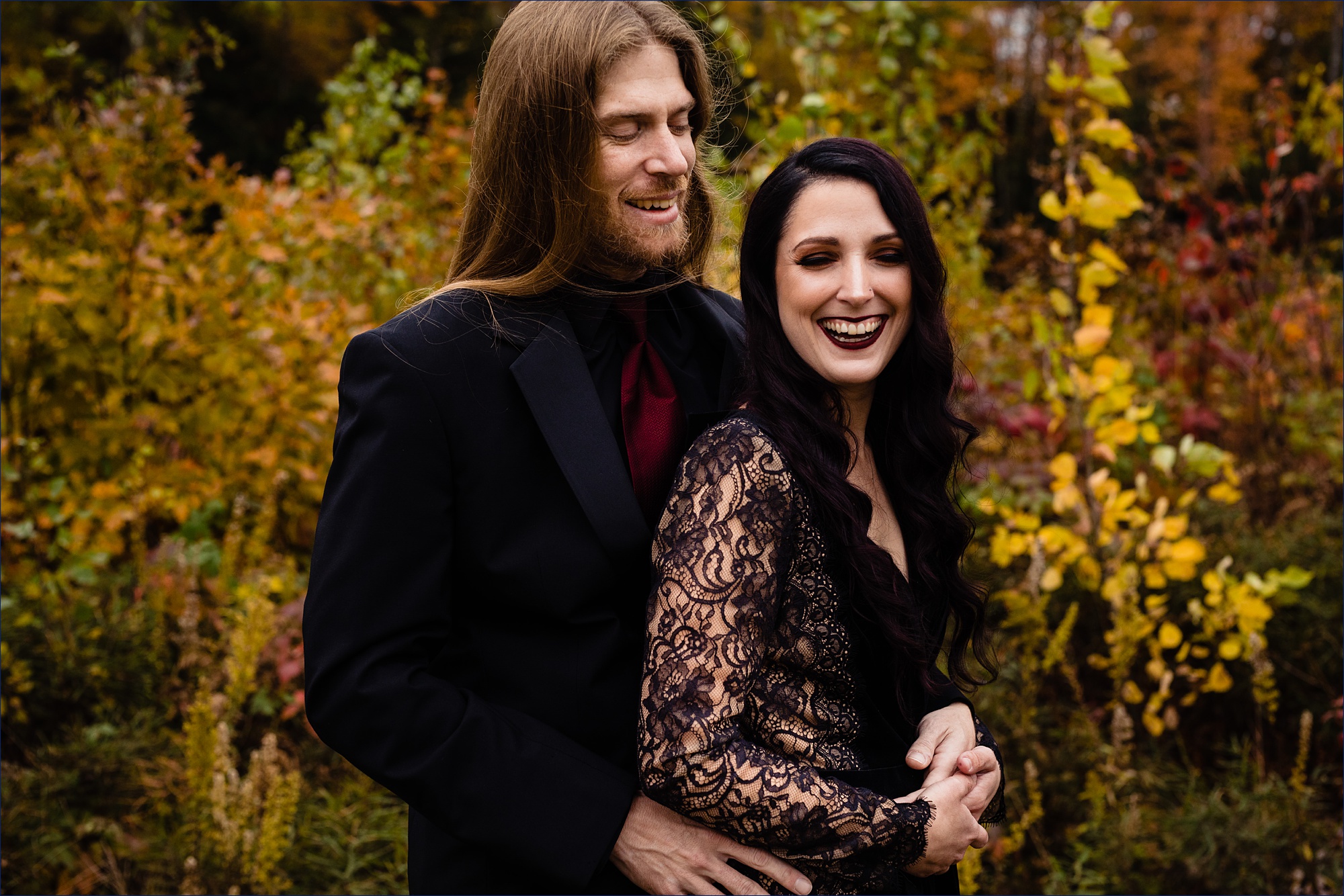 The bride and groom smile together in the fall colored trees for their Halloween inspired New Hampshire wedding day