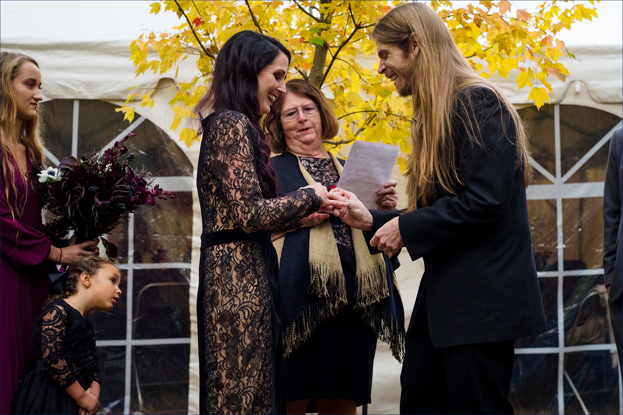 The bride and groom exchange wedding rings at their fall outdoor wedding ceremony