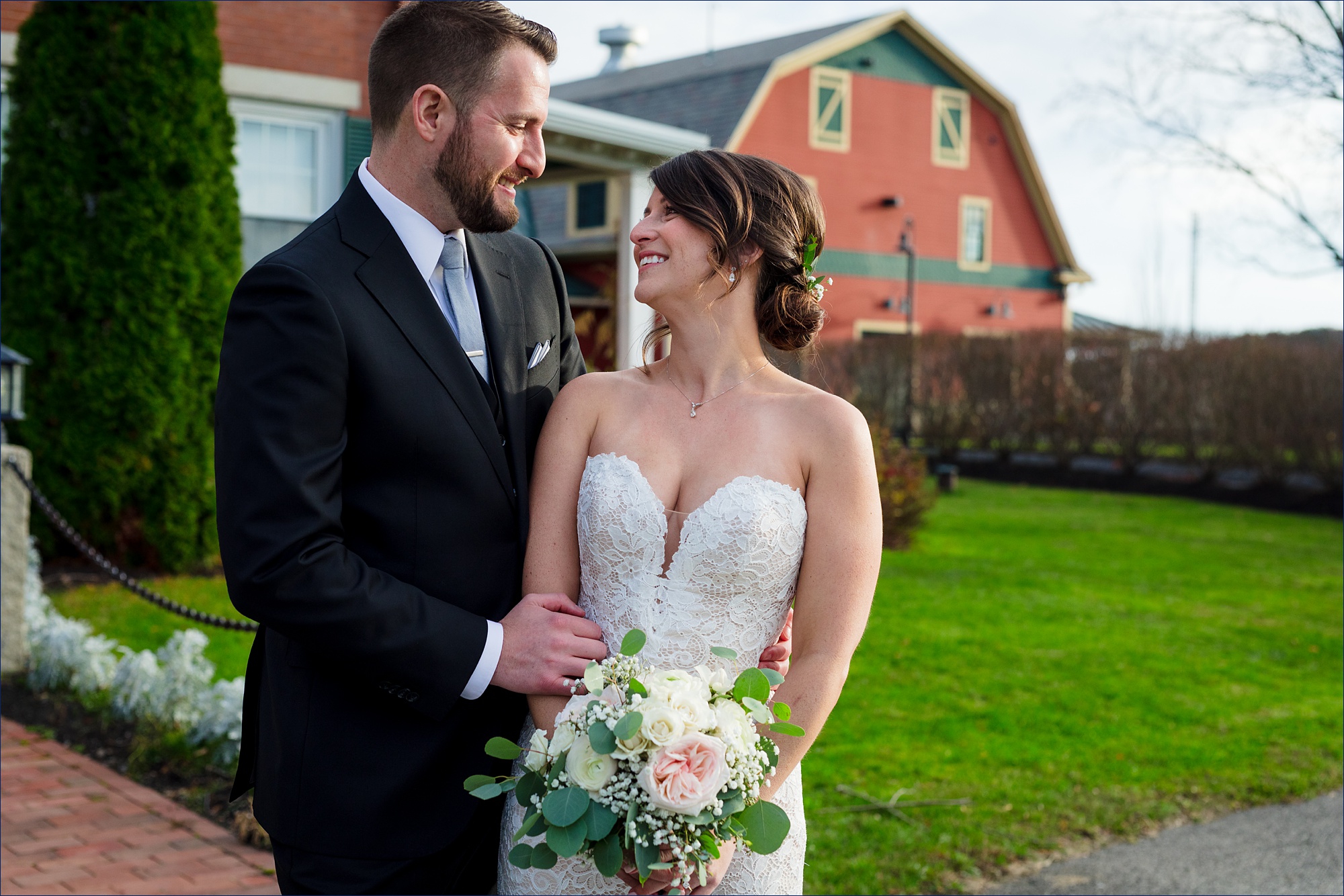 The newlyweds laugh together in front of the Red Barn at Outlook Farm