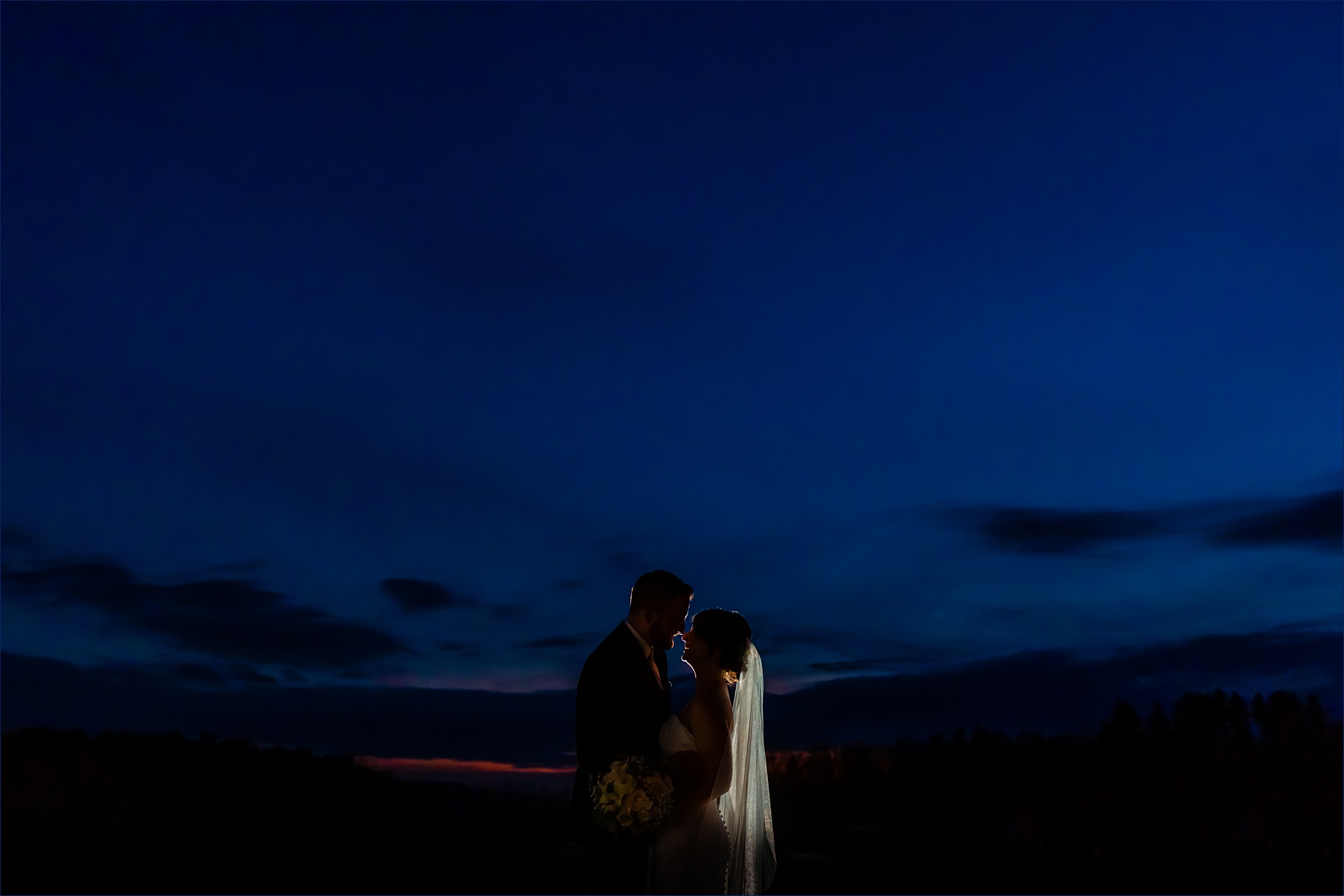 The newlyweds are silhouetted against the deep blue southern Maine sky at their Red Barn at Outlook Farm wedding day