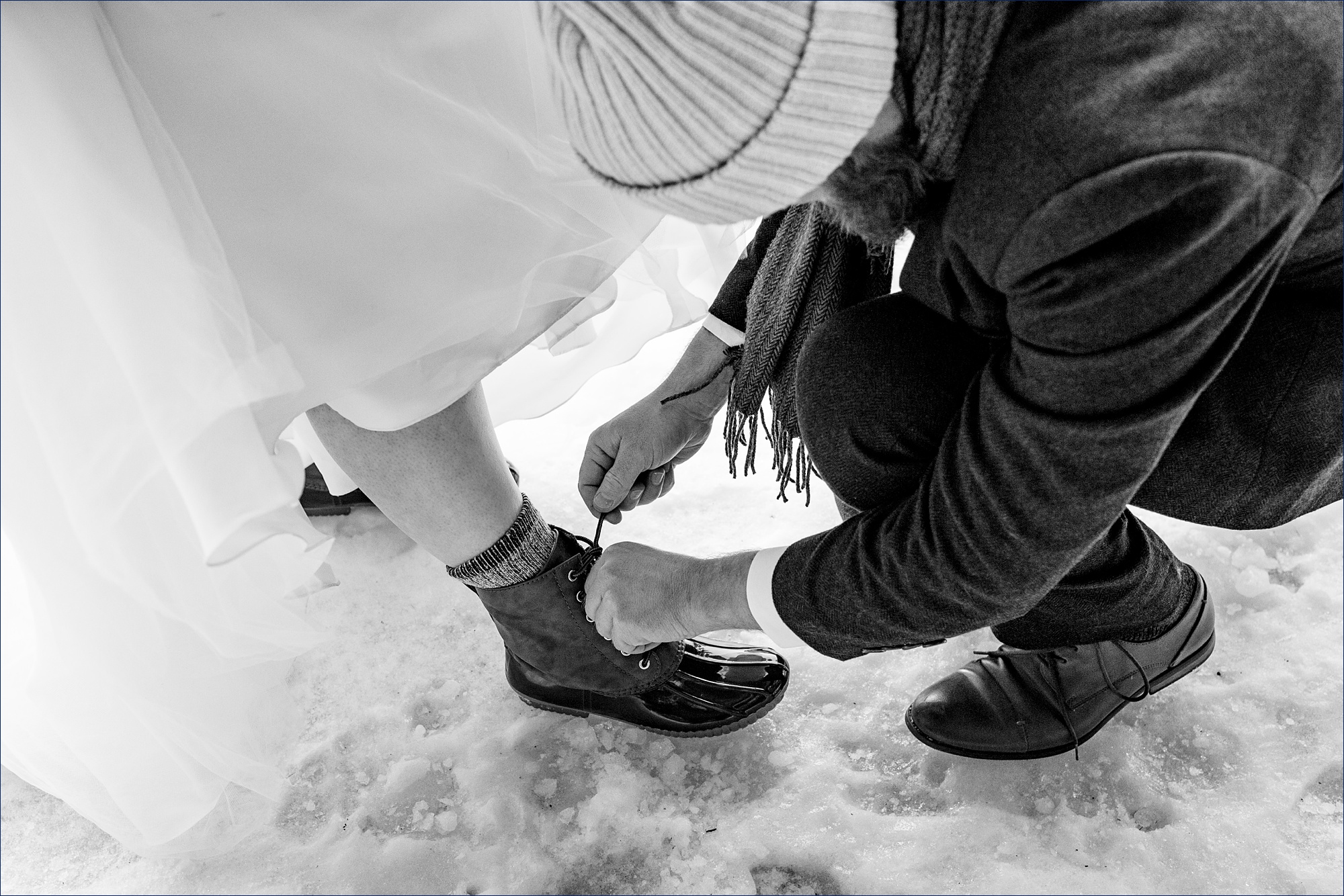 The groom ties the bride's boots for her on their winter NH elopement