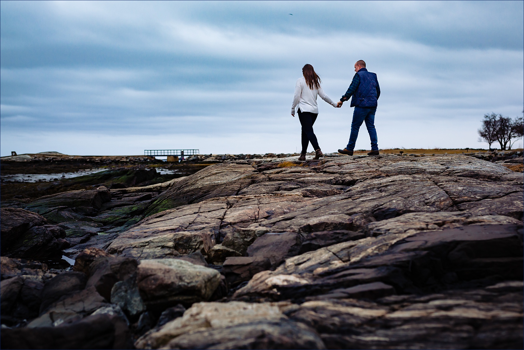The couple walks hand in hand on the rocky shores of the Great Island Common NH 