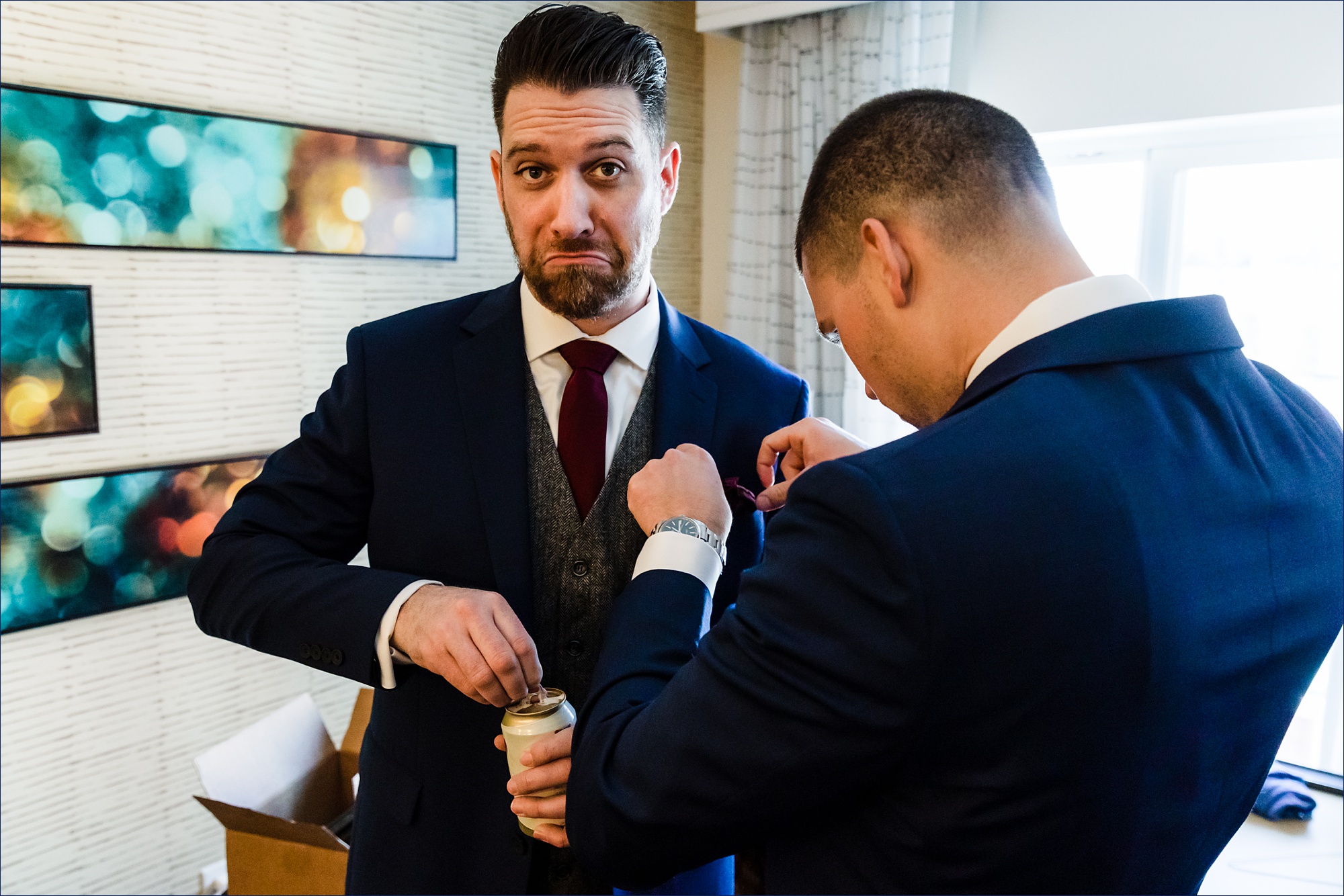 The groom cracks open a cold one while a groomsman gets his pocket square set