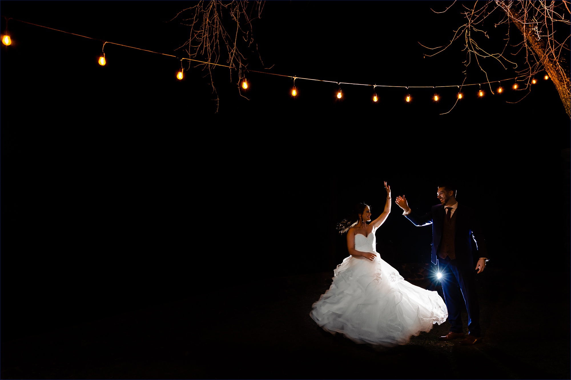 The groom gives the bride a spin on their wedding day under the twinkle lights