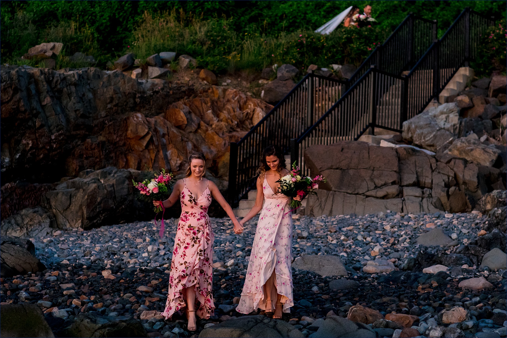 The bride's sisters walk out on the rocky beach as the bride comes down the stairs to the sunrise beach elopement in Maine