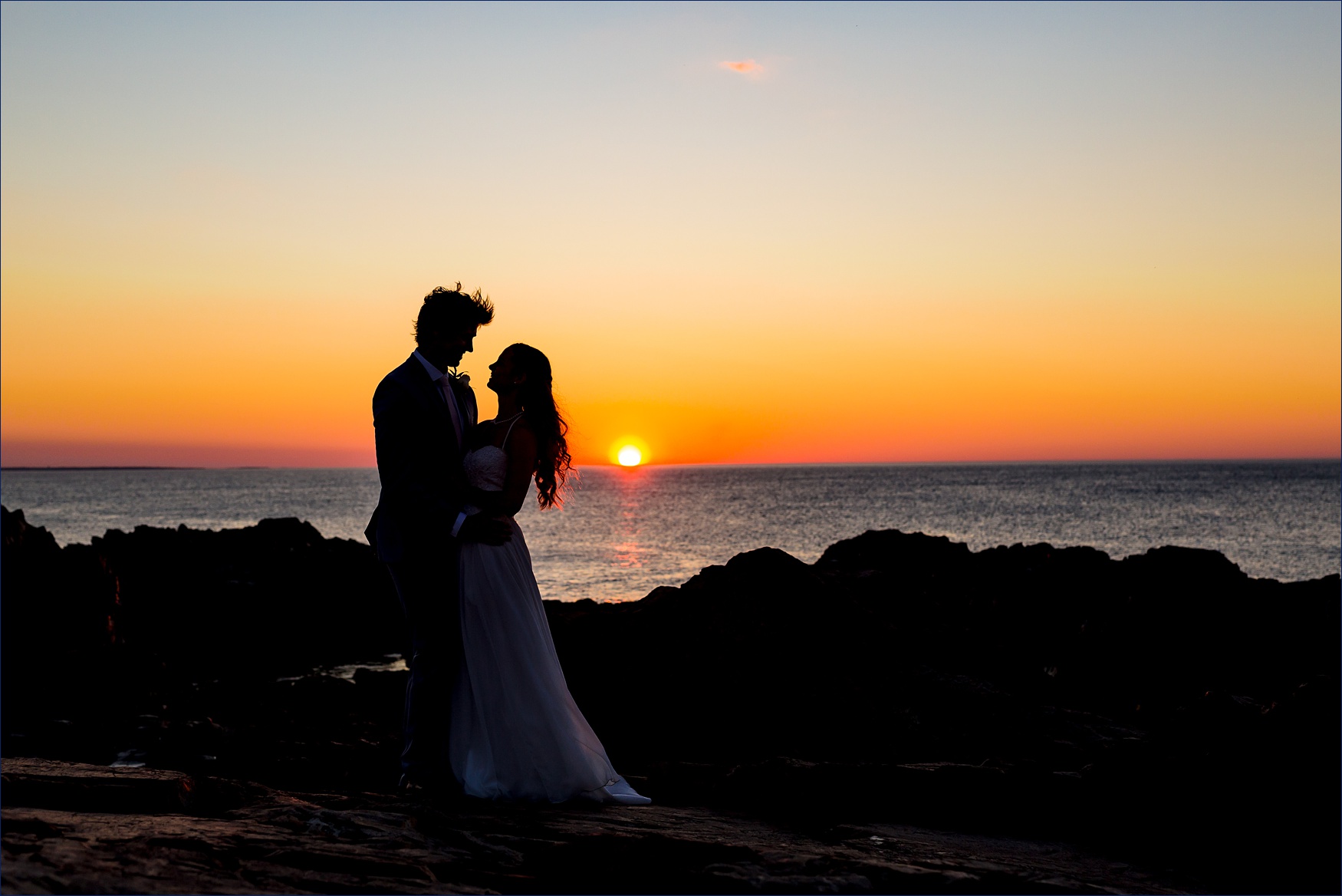 The bride and groom stand in front of the sunrise while out on the Marginal Way rocks after eloping
