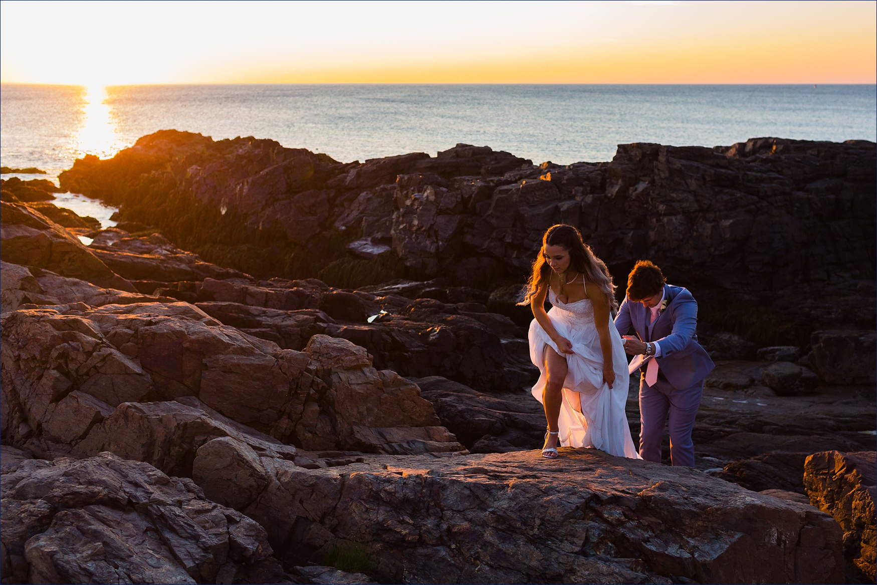The groom helps the bride out on the rocks at Marginal Way