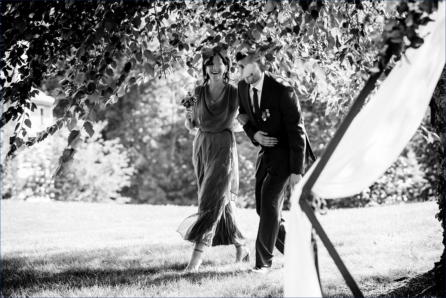 The groom and his mom peek through the trees as he goes to enter the backyard intimate wedding ceremony