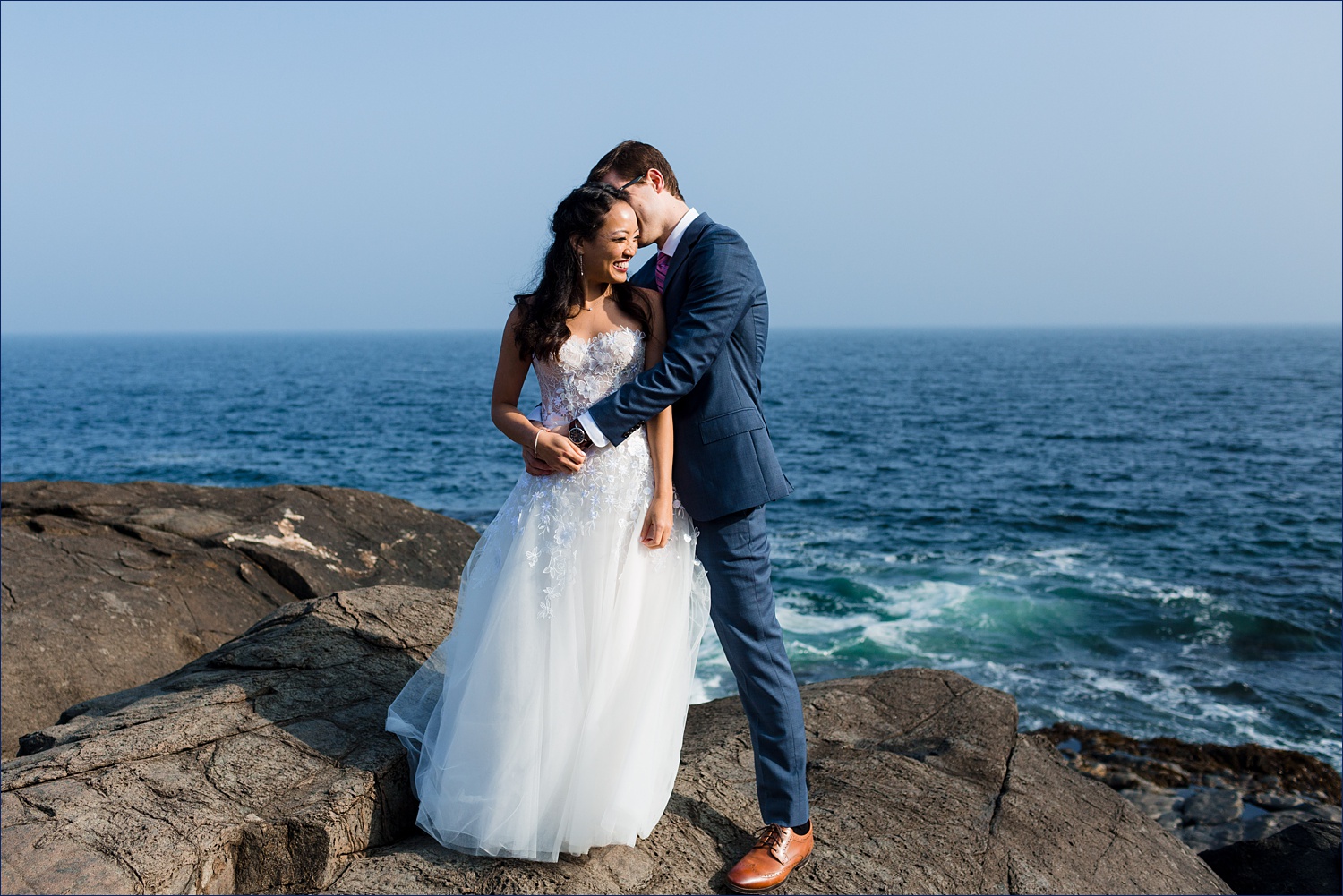 The newlyweds laugh together on the rocky shore of Ogunquit Maine