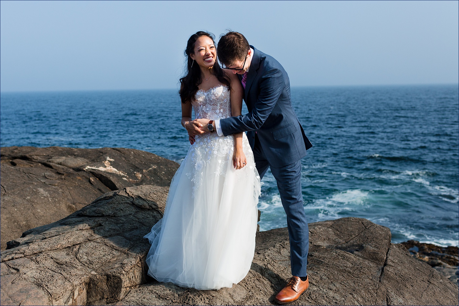 The newlyweds laugh together on the rocky shore of Ogunquit Maine