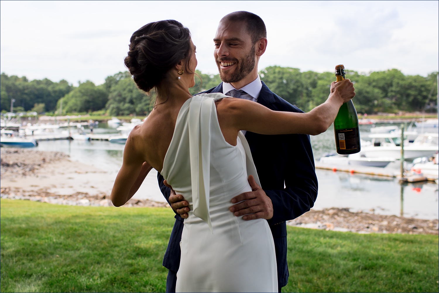 THe bride greets the groom for their first look with a bottle of champagne on their Maine Wedding day