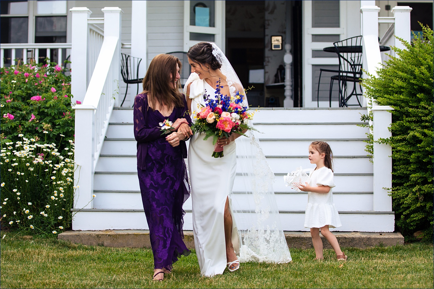 The mother of the bride walks her daughter down the aisle as a flower girl jumps back in to dump more petals in York Maine