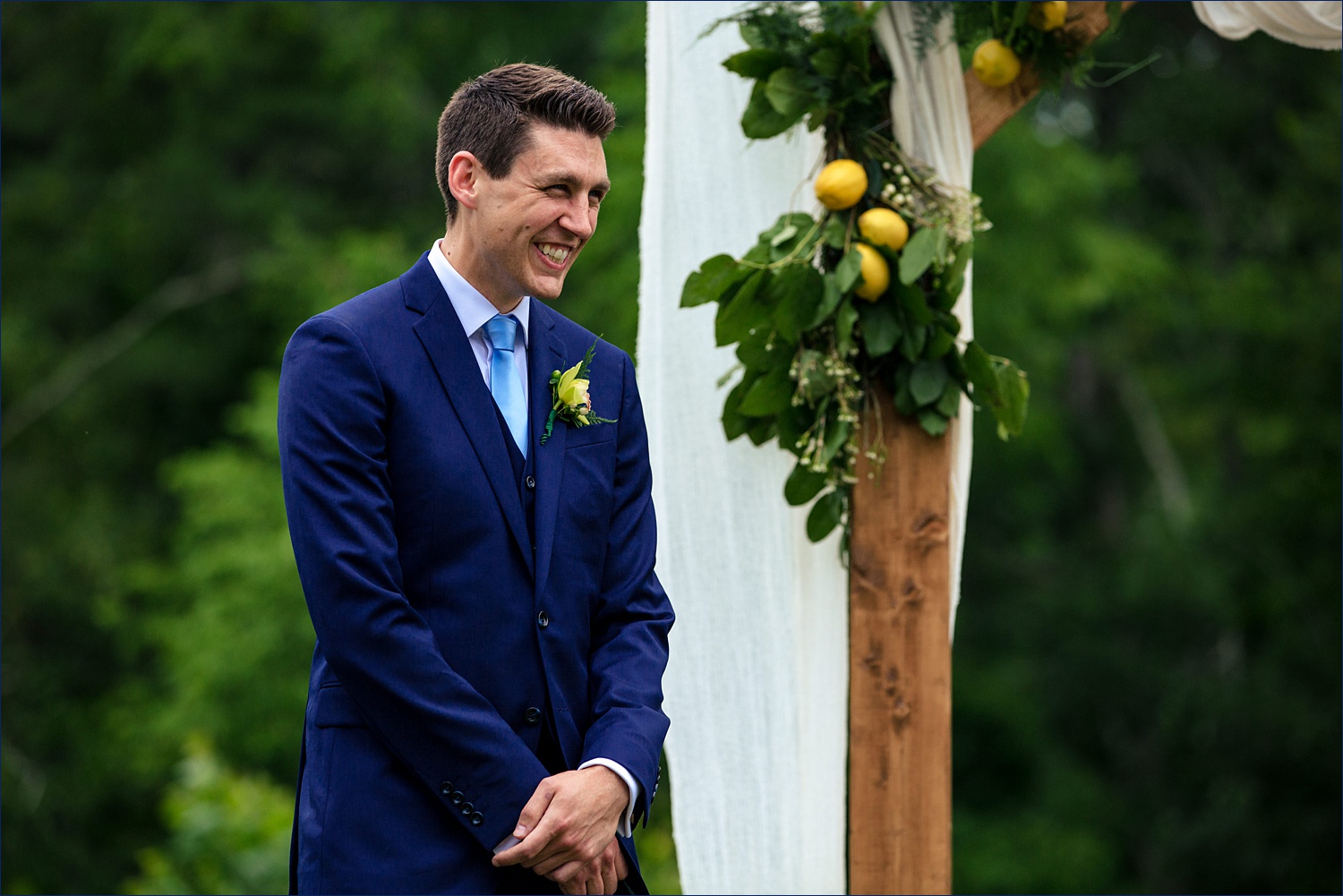 The groom smiles big at the bride during their outdoor wooded ceremony