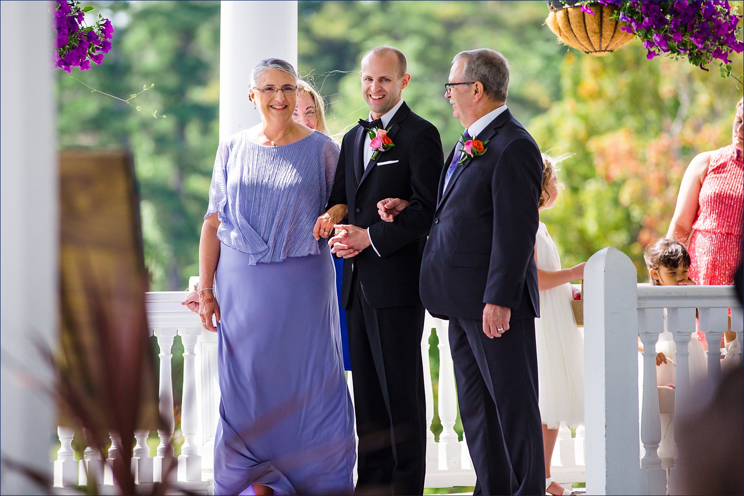 The groom stands with his parents as the start to walk him into the wedding ceremony on the veranda