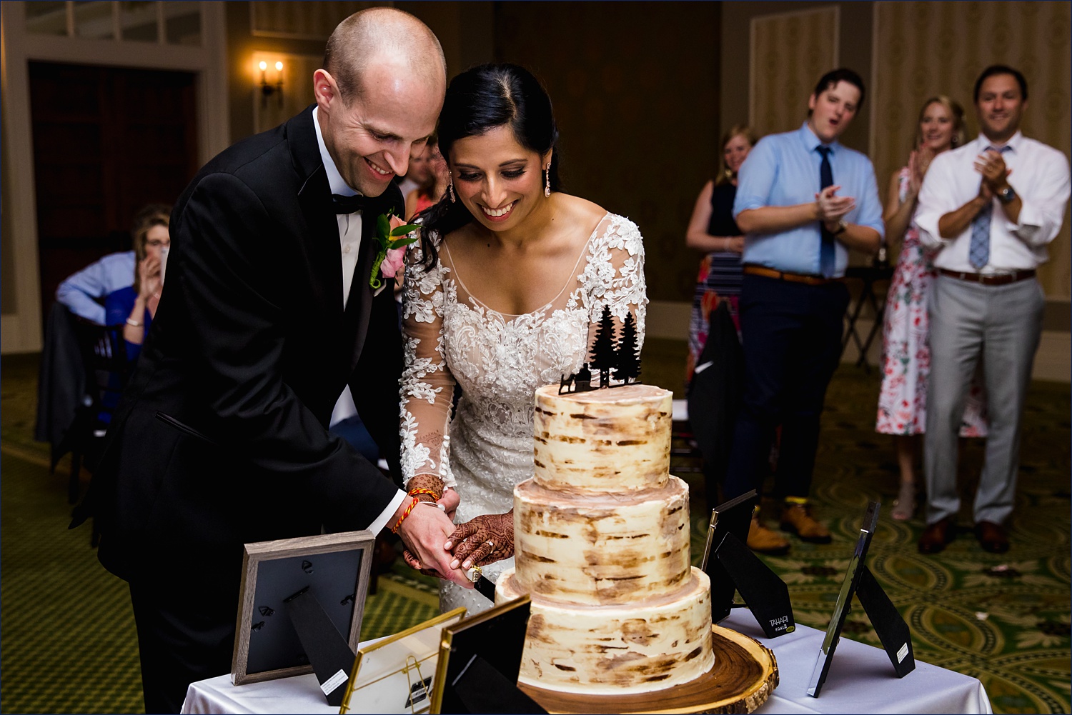The bride and groom cut their wedding cake while family cheers them on