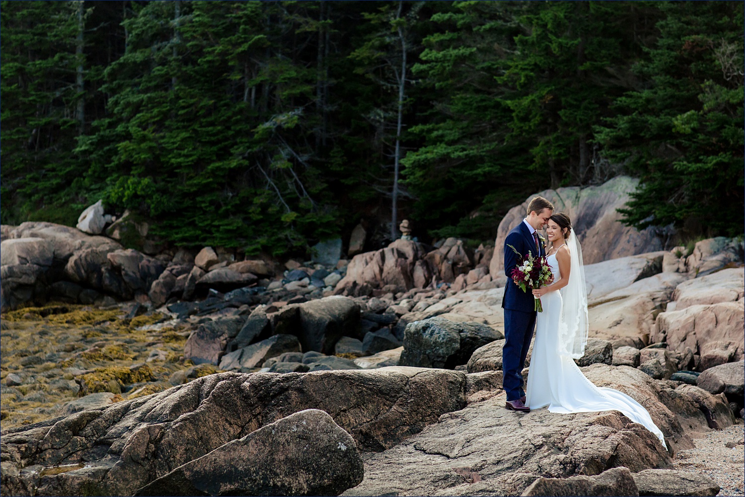 The newlyweds laugh together in front of the majestic coastal Maine woods