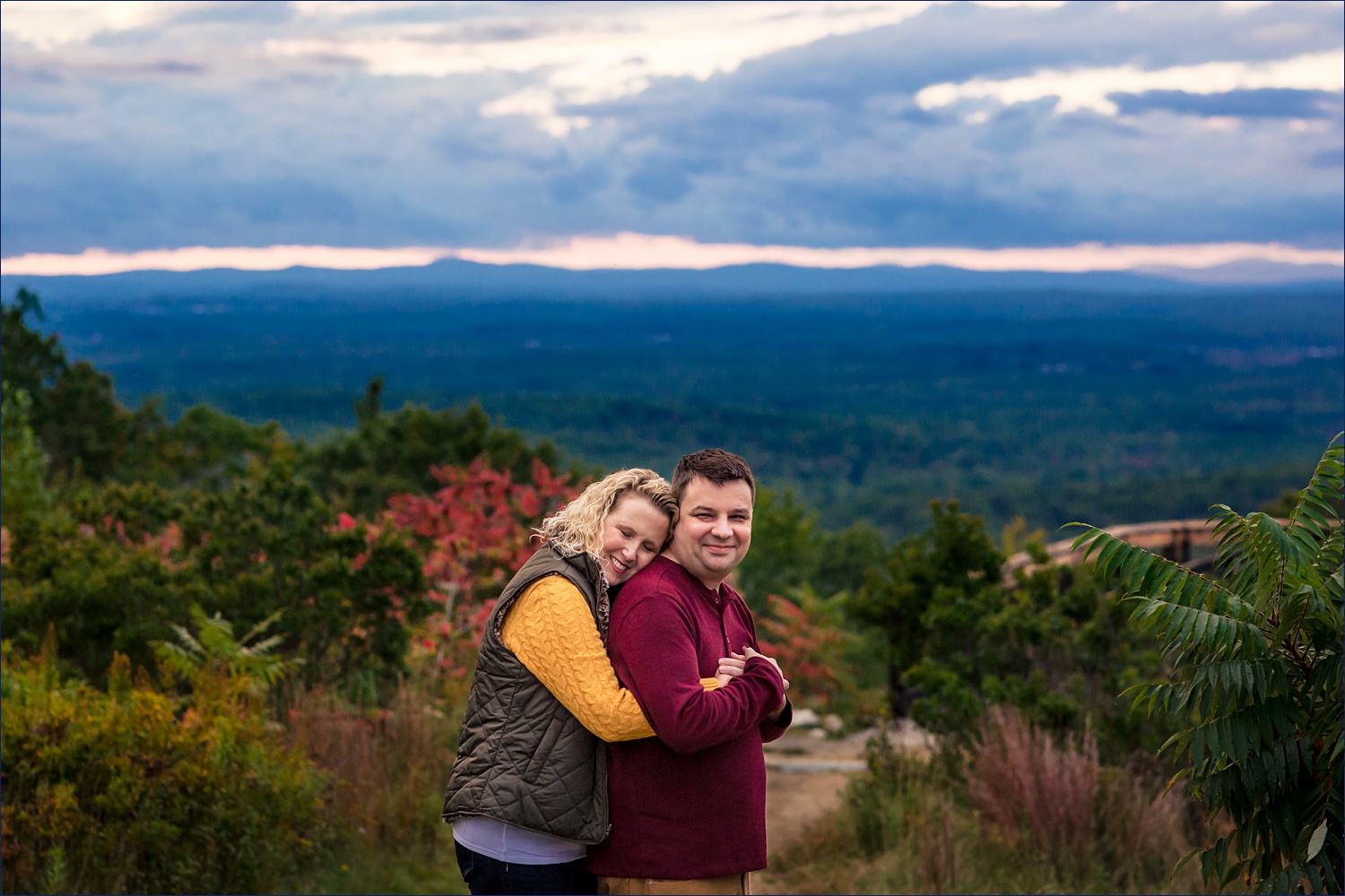 She squeezes him tight in a bear hug at their fall Maine engagement session