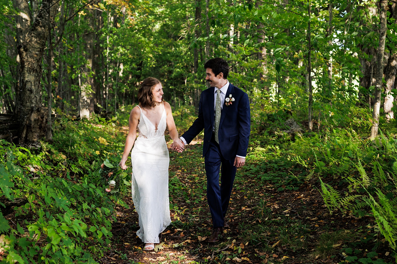 The couple walk down a wooded path on their wedding day