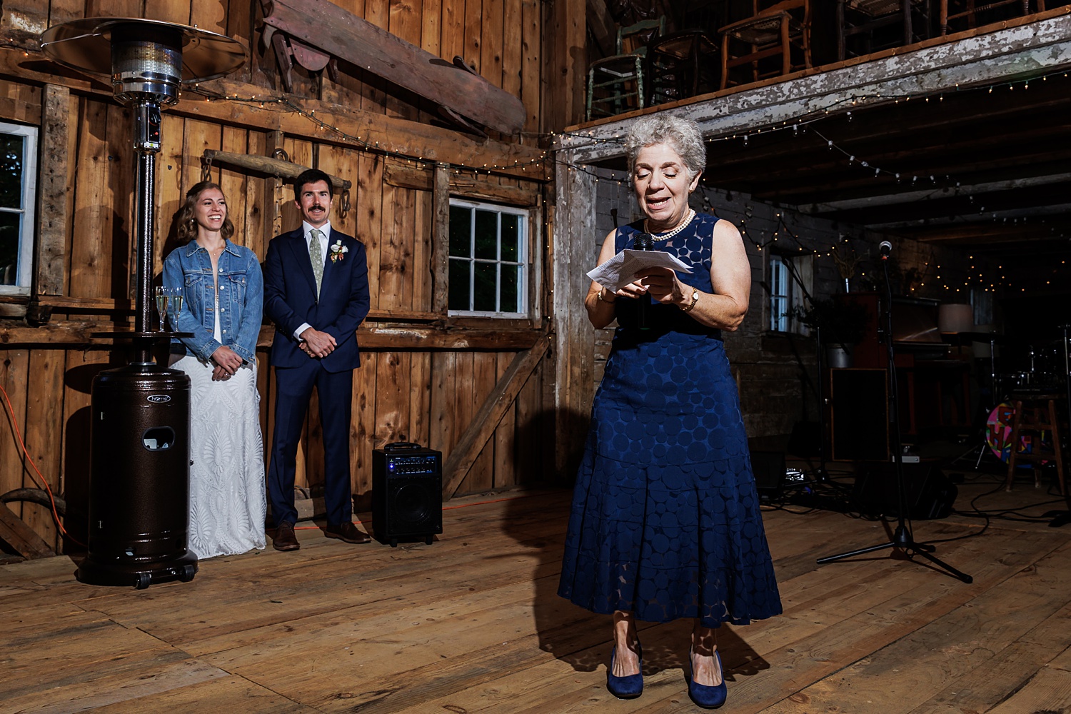The couple listens to toasts at their barn wedding reception