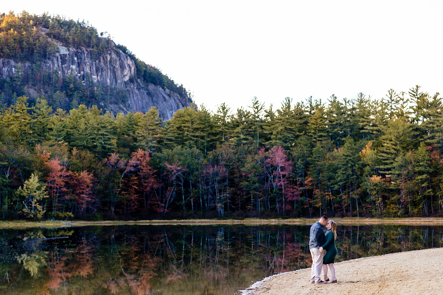 Sharing a kiss in front of Echo Lake NH for their engagement session in the White Mountains