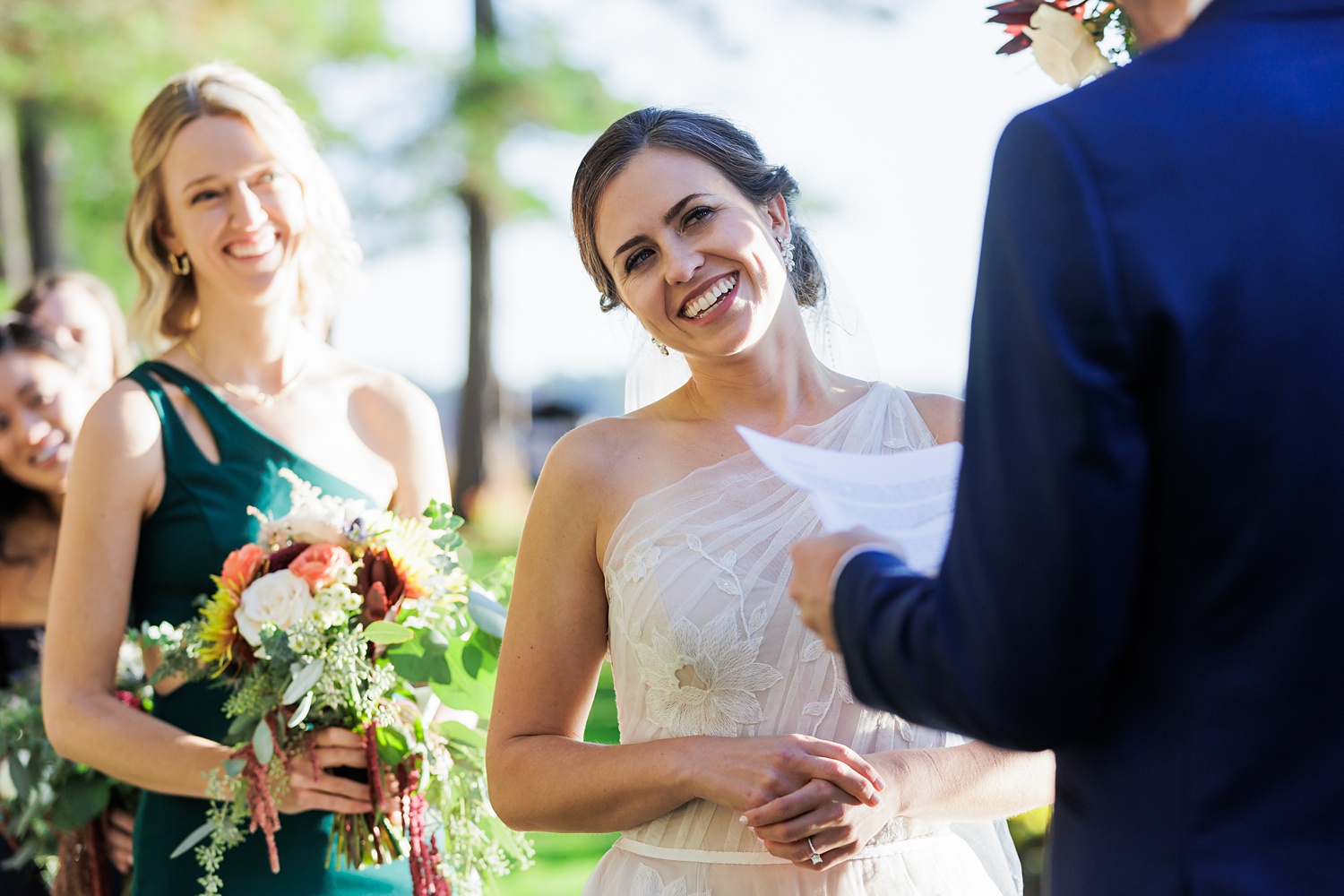 The bride smiles warmly at her husband during the wedding ceremony outside on a fall Maine day