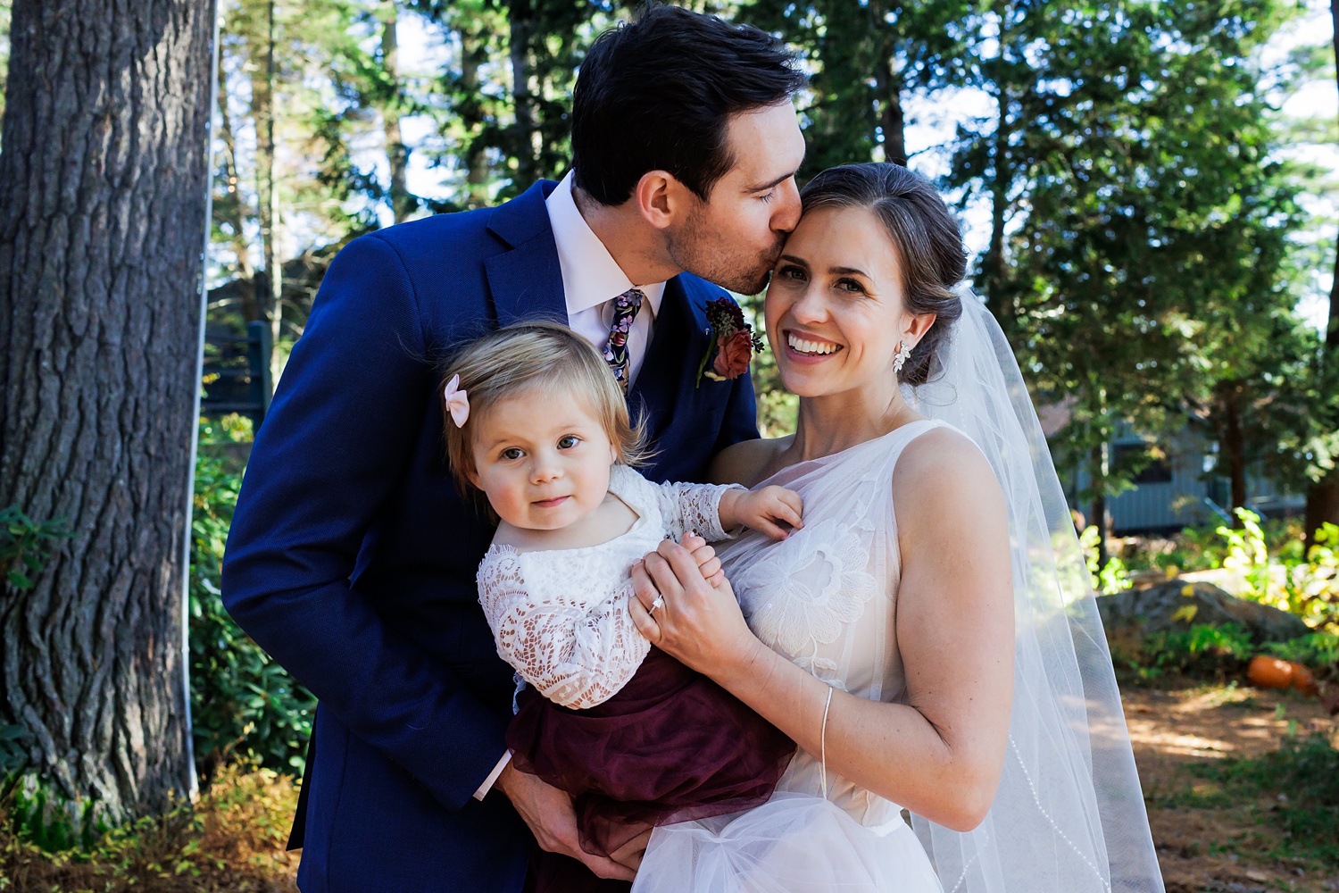 The couple and their young daughter share a moment together on the wedding day in Maine