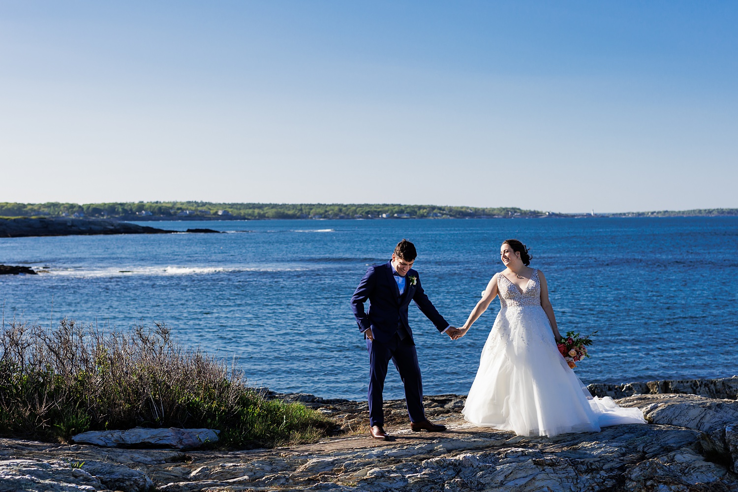 Bride and groom laugh and hold hands with Portland Maine and the ocean in the background