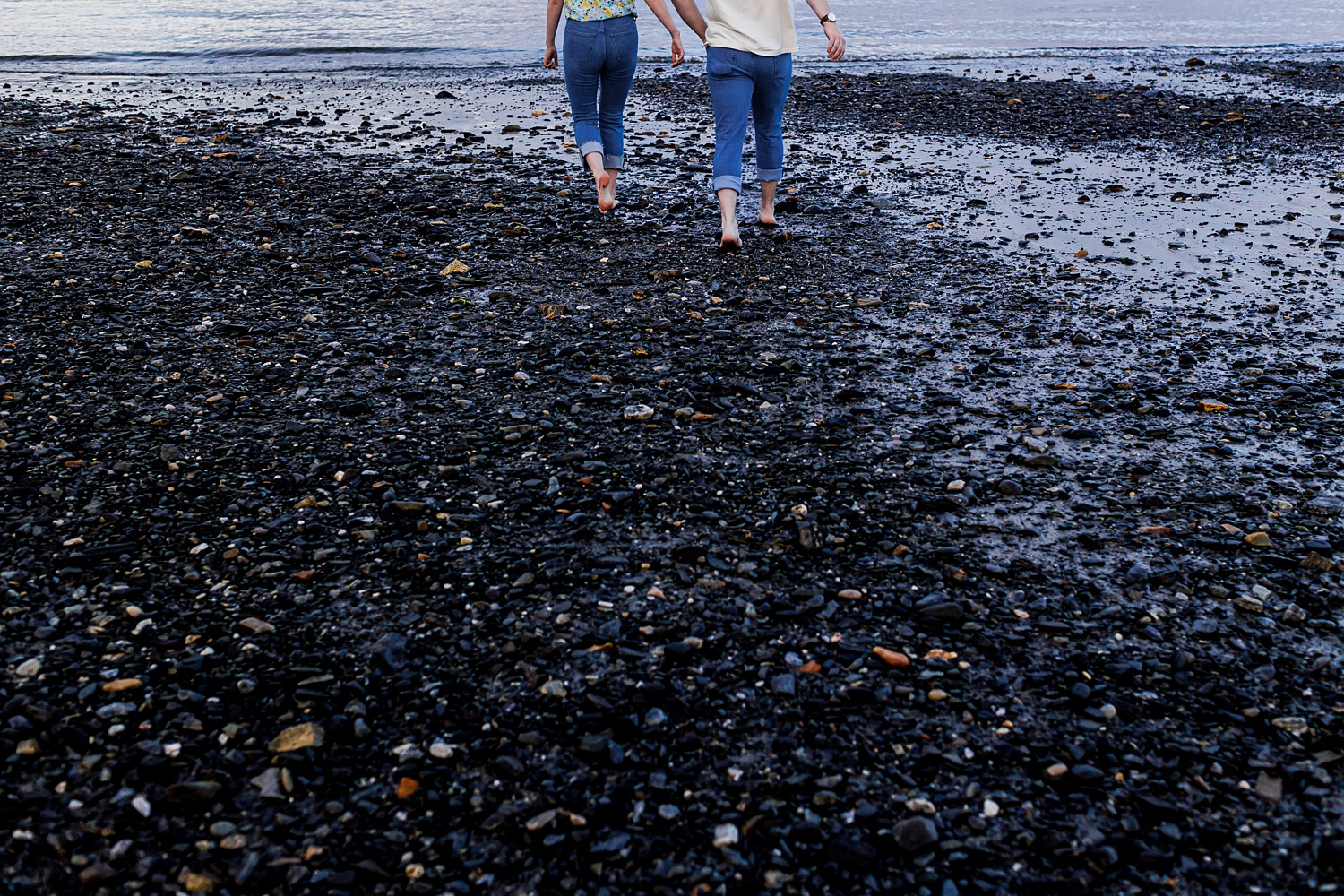 The couple walks on the rocky shores to the ocean water in New Hampshire