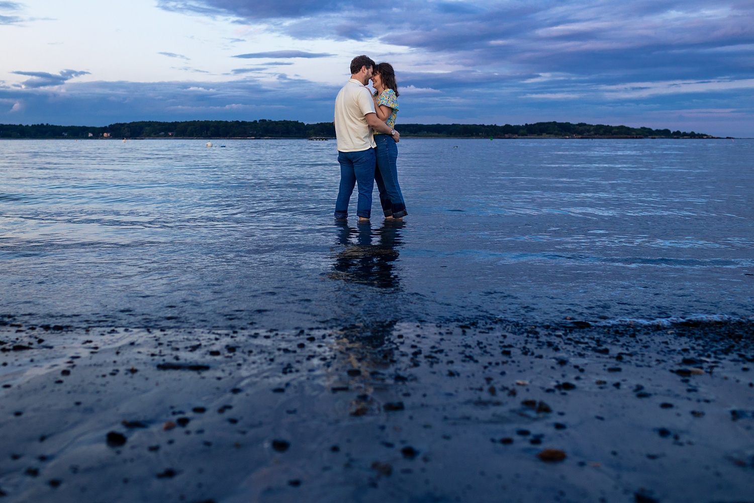 The couple stands with their feet in the cold ocean water at Great Island Common NH